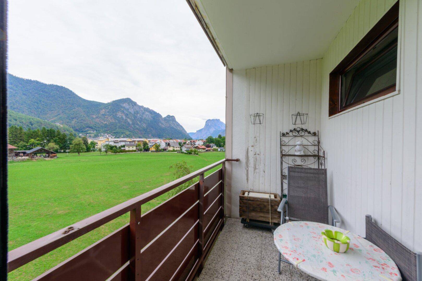 Geräumiger Balkon mit Blick auf eine weite grüne Wiese und die beeindruckende Berglandschaft.