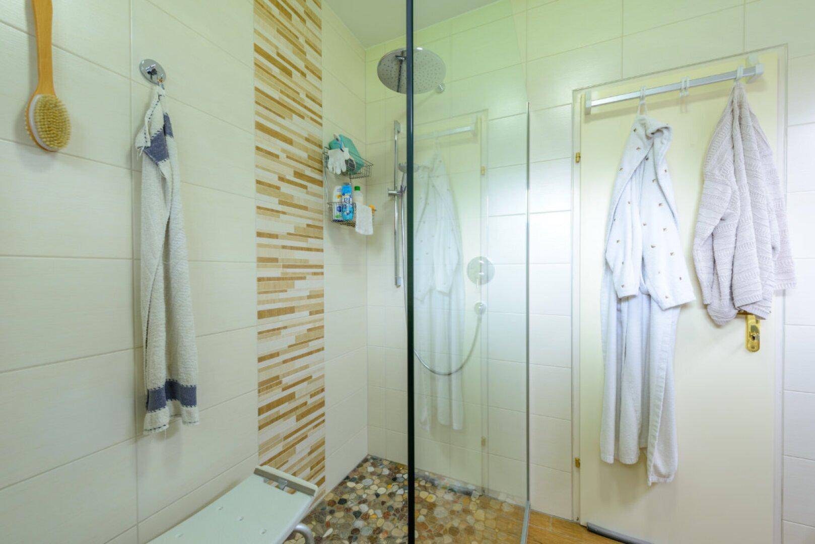 Duschbereich mit Glasabtrennung, modernen Fliesen und einem dekorativen Kiesboden in der Dusche.