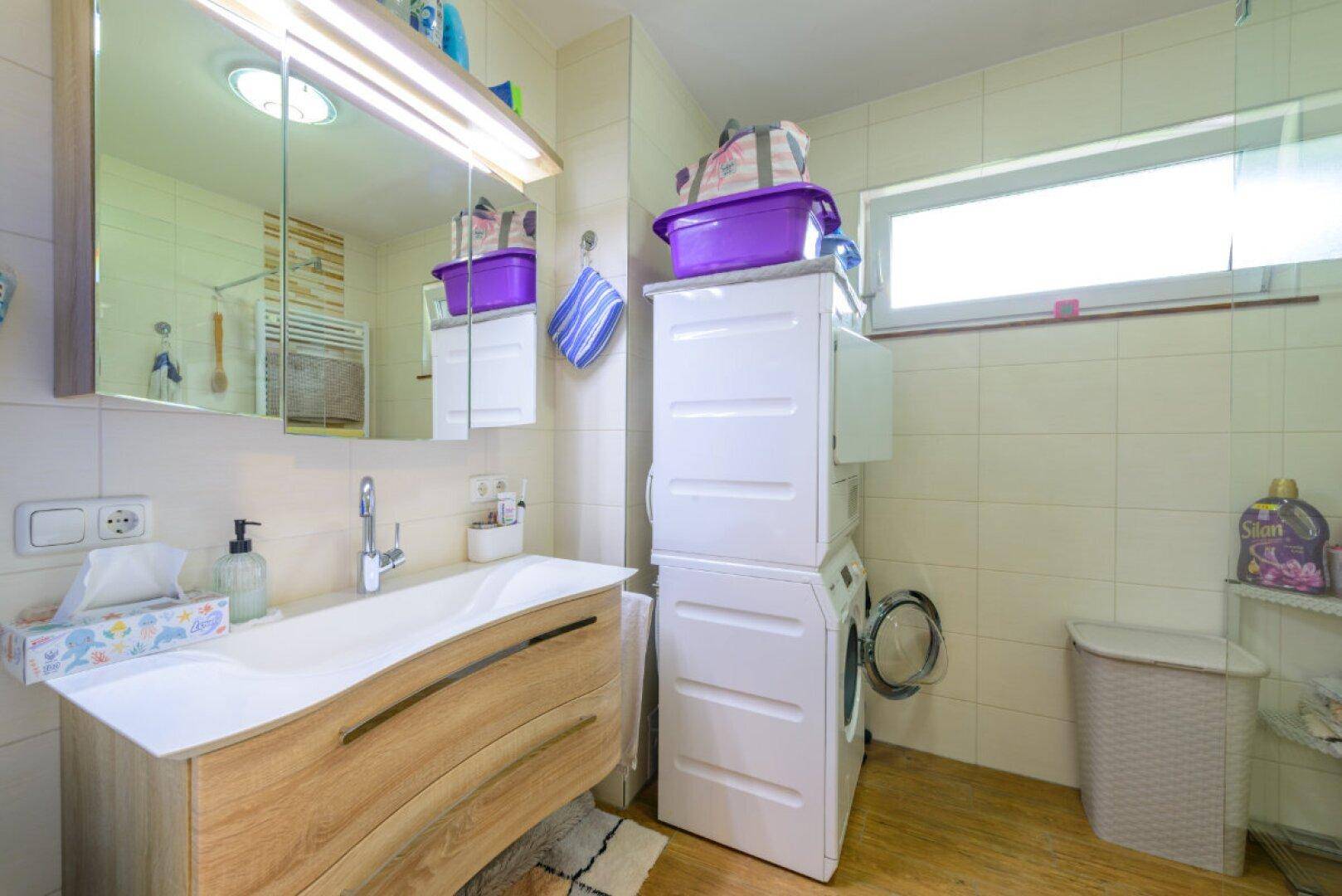 Modernes Badezimmer mit Waschbecken, Waschmaschine und Trockner sowie einem Fenster für Tageslicht.
