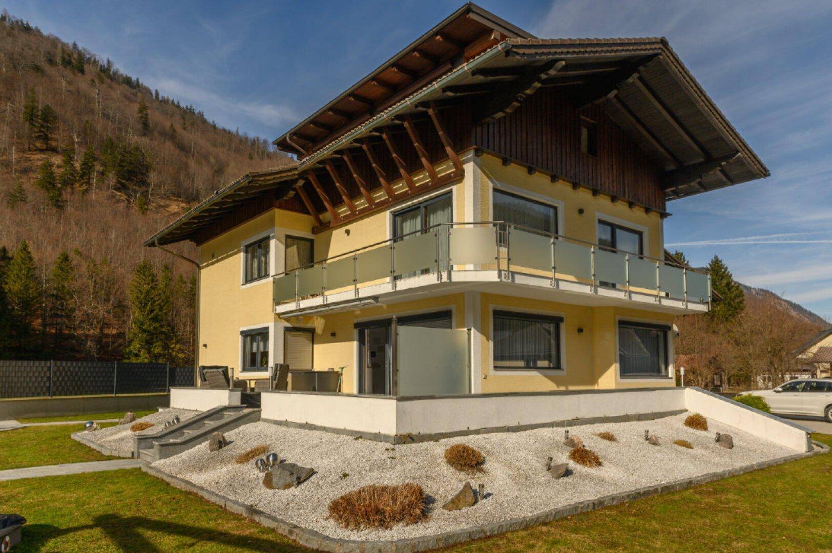 Ansicht des Hauses mit Balkonen, Terrassen und gepflegtem Garten vor Bergkulisse.