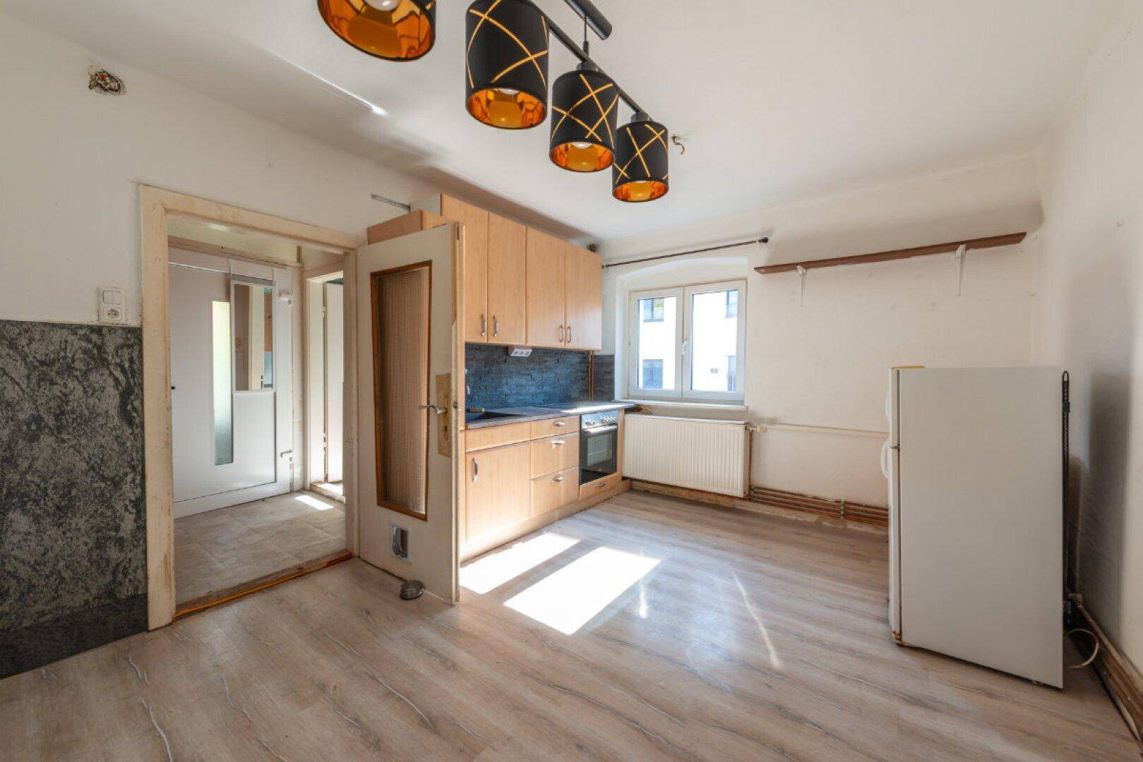 Küche mit älteren Holzschränken, Herd und Kühlschrank, die Renovierungsbedarf aufweist.