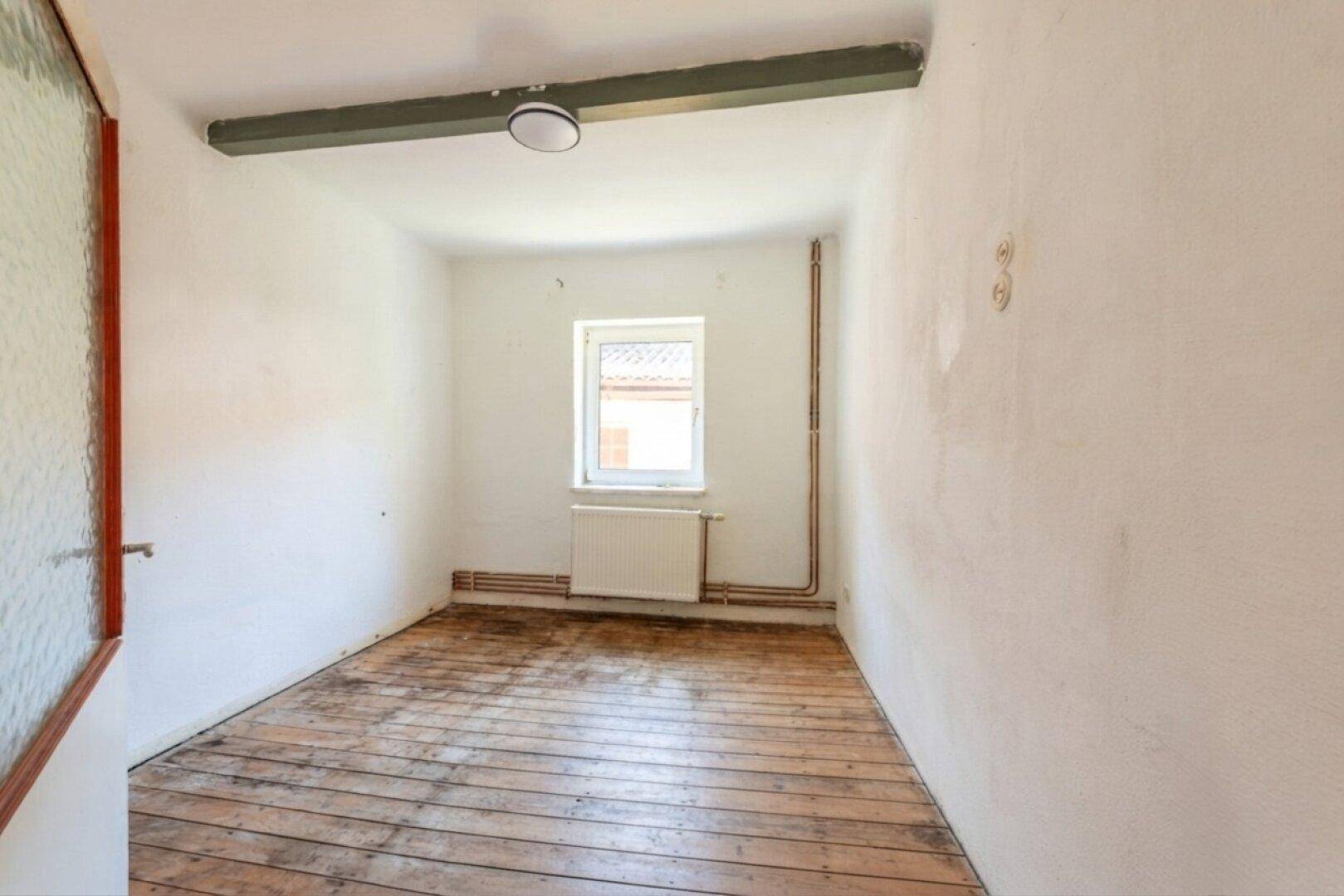 Leerer Raum mit abgenutztem Holzboden und Fenster, der auf eine Renovierung wartet.