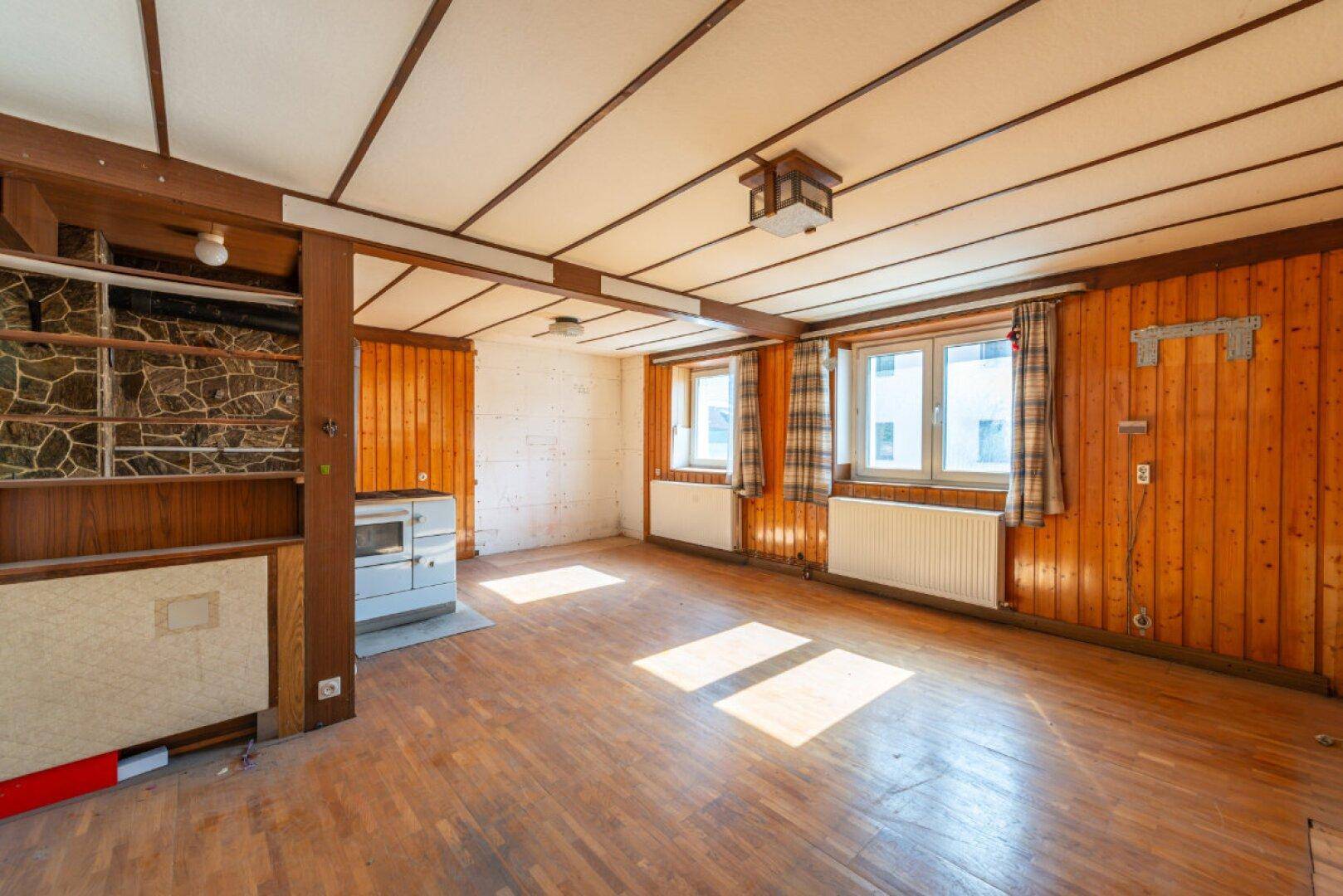 Wohnzimmer mit Holzboden, Holzvertäfelung und Fenstern, die viel Tageslicht hereinlassen.