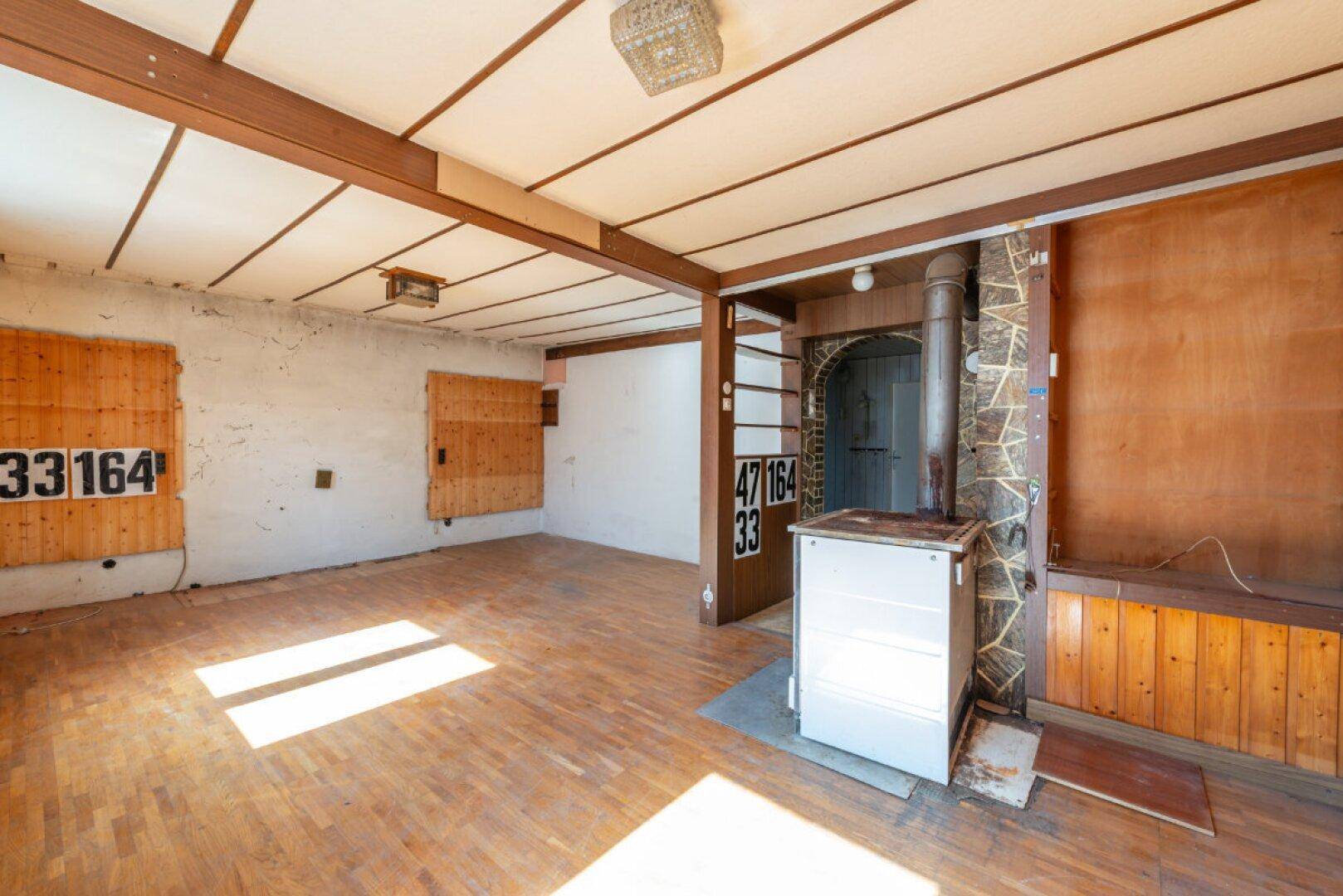 Geräumiges Wohnzimmer mit Parkettboden, Holzdecke und einem traditionellen Kachelofen.