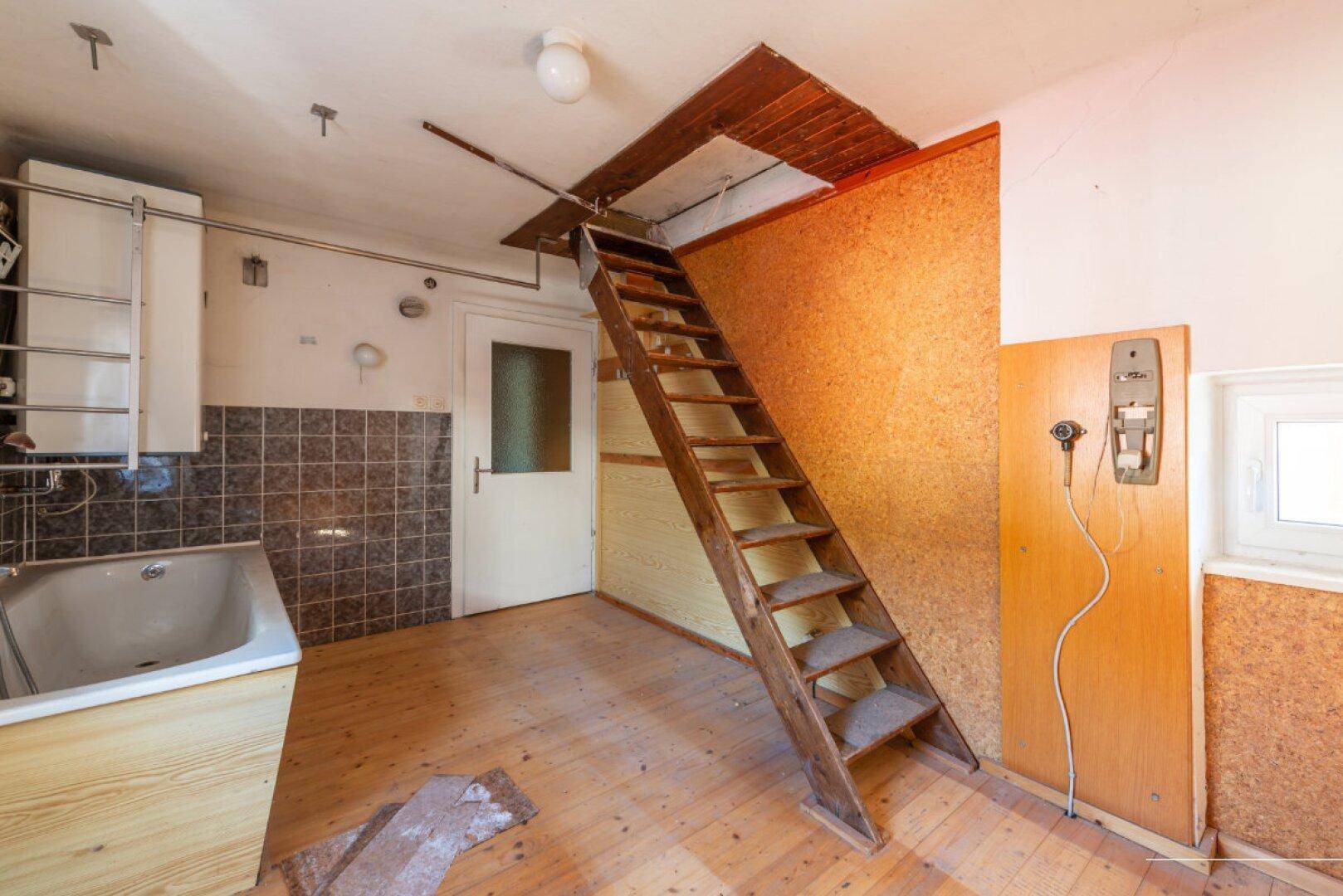 Badezimmer mit Badewanne, Warmwasserbereiter und einer Holzleiter, die zum Dachboden führt.