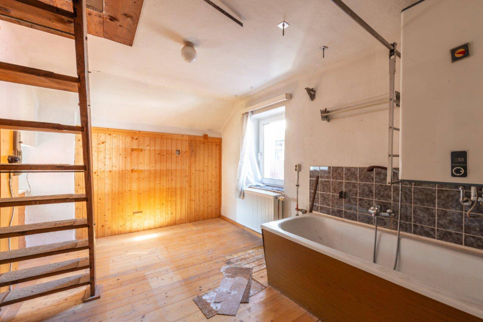 Badezimmer mit Badewanne, gefliester Wand und Holzleiter, die zu einem oberen Bereich führt.