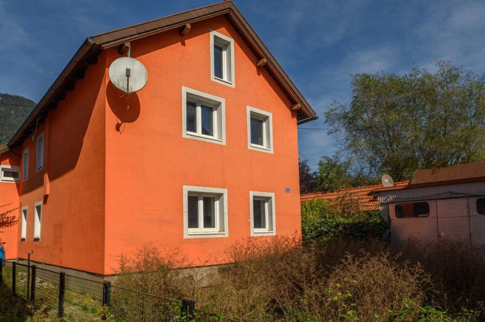 Seitenansicht des Wohnhauses mit leuchtend oranger Fassade und Satteldach unter blauem Himmel.