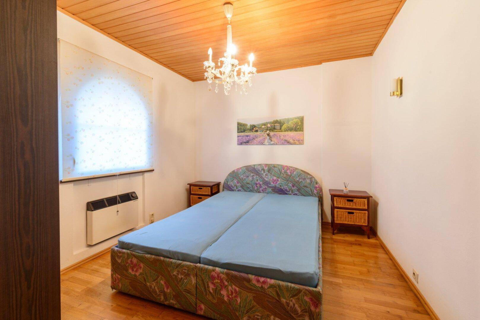Schlafzimmer mit Holzboden, Kronleuchter und traditionellem Bett mit floralem Muster.
