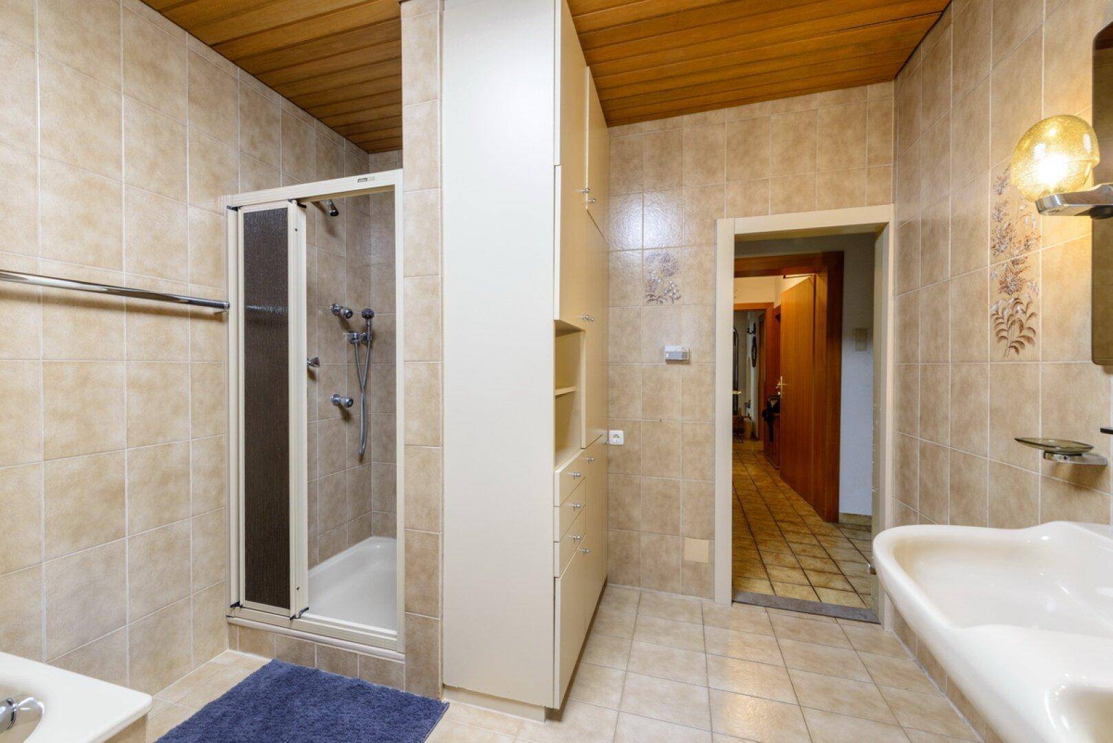 Badezimmer mit Duschkabine, beigefarbenen Fliesen und praktischen Einbauschränken.