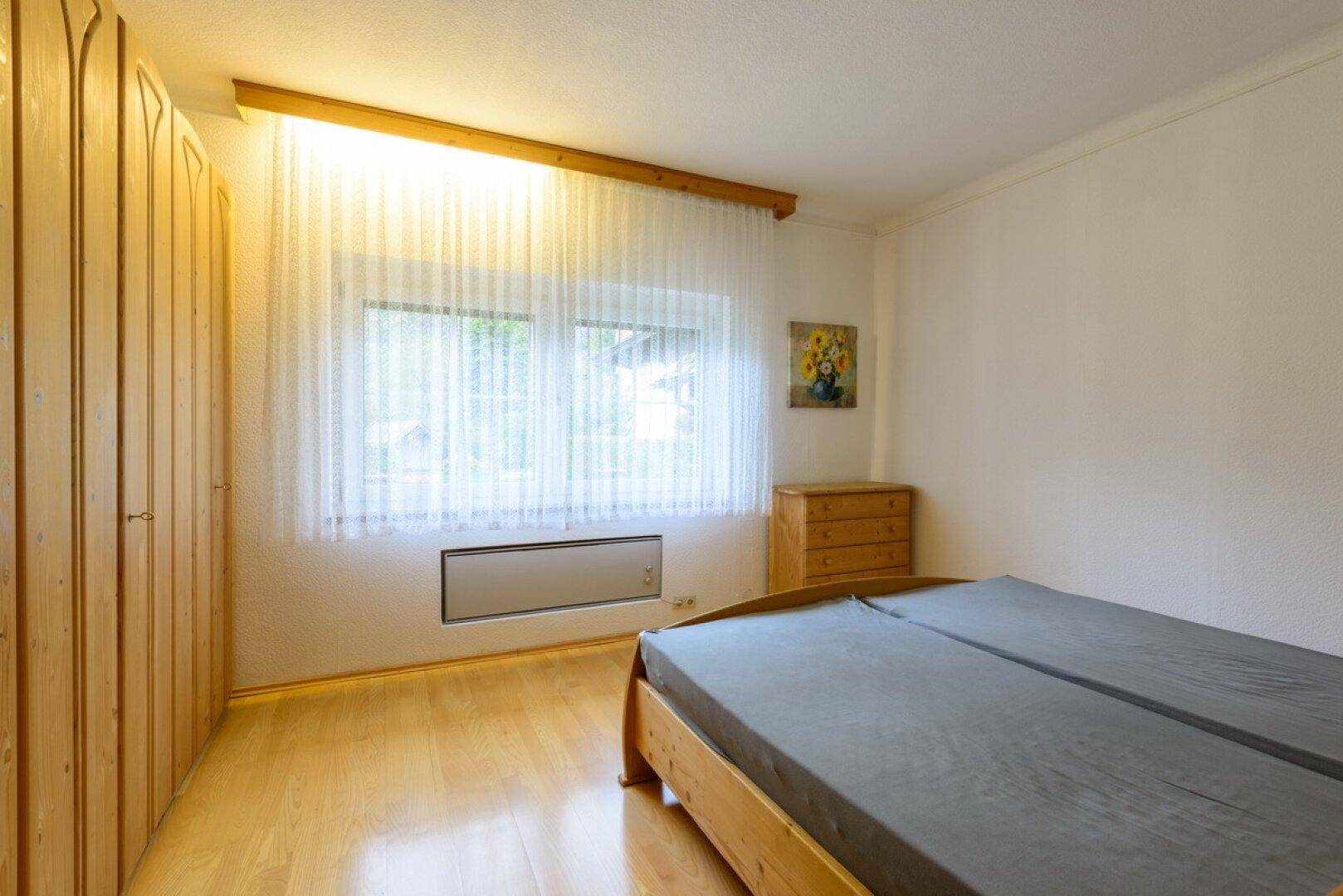 Schlafzimmer mit Holzboden, Einbauschränken und Fenster mit Blick ins Grüne.