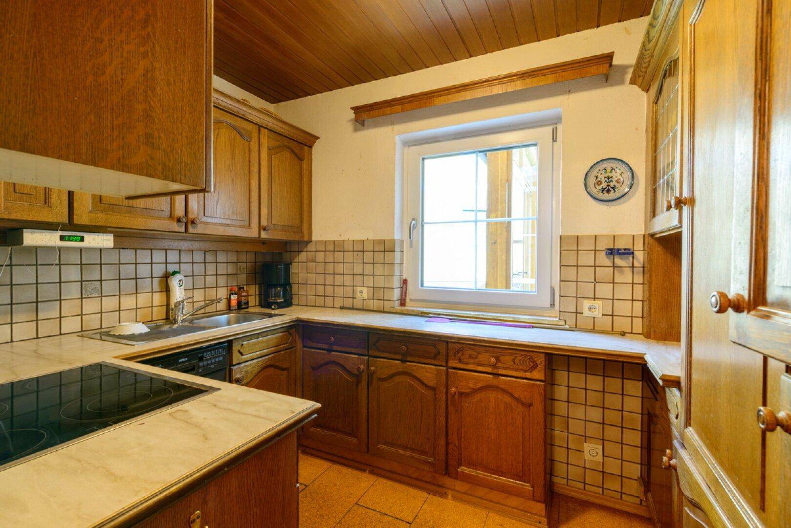 Rustikale Küche mit Holzschränken, Fliesenrückwand und integriertem Kochfeld.