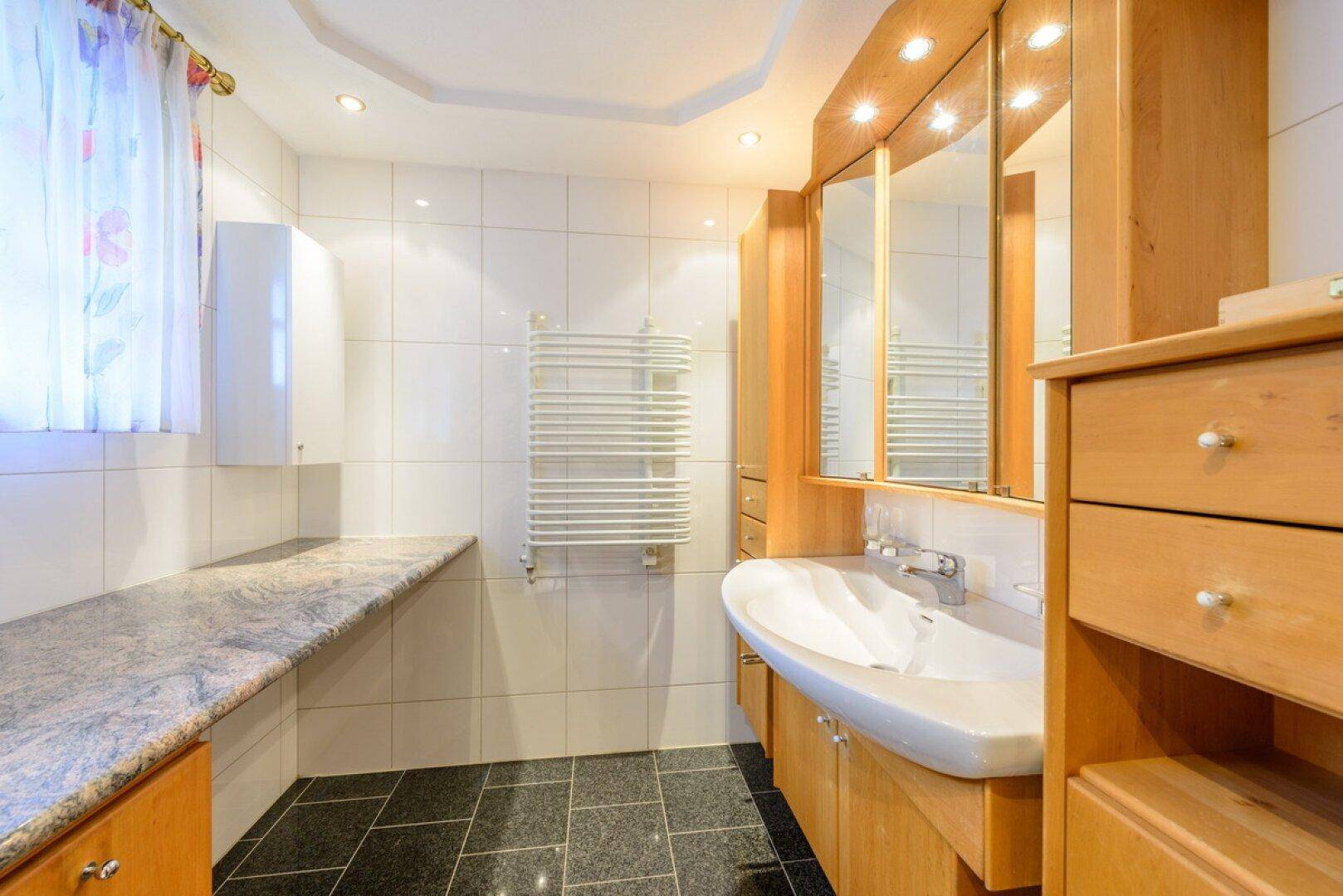 Badezimmer mit Waschtisch, Spiegelschrank, Granitablage und beheiztem Handtuchhalter.