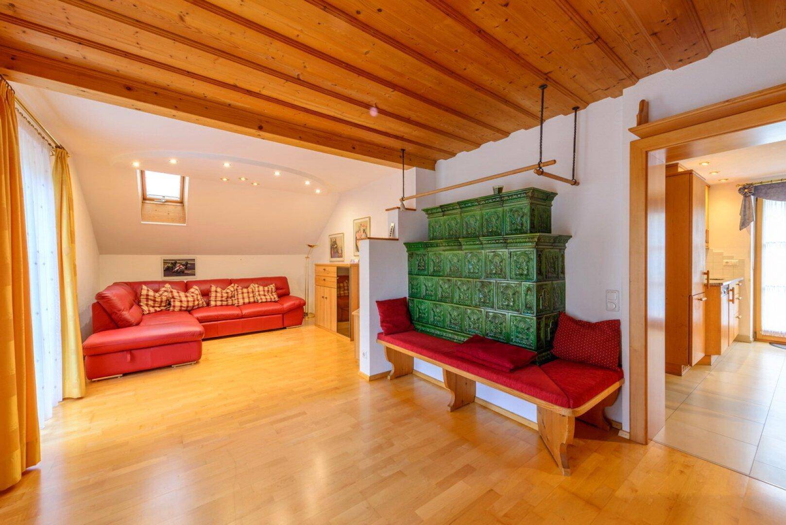 Gemütliches Wohnzimmer mit Holzbalkendecke, Parkettboden und traditionellem Kachelofen.