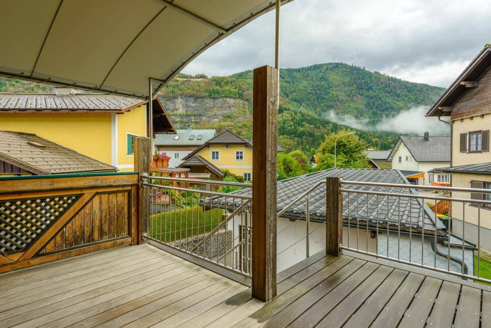Geräumige Holzterrasse mit Überdachung und Blick auf die grüne Umgebung und Berge.