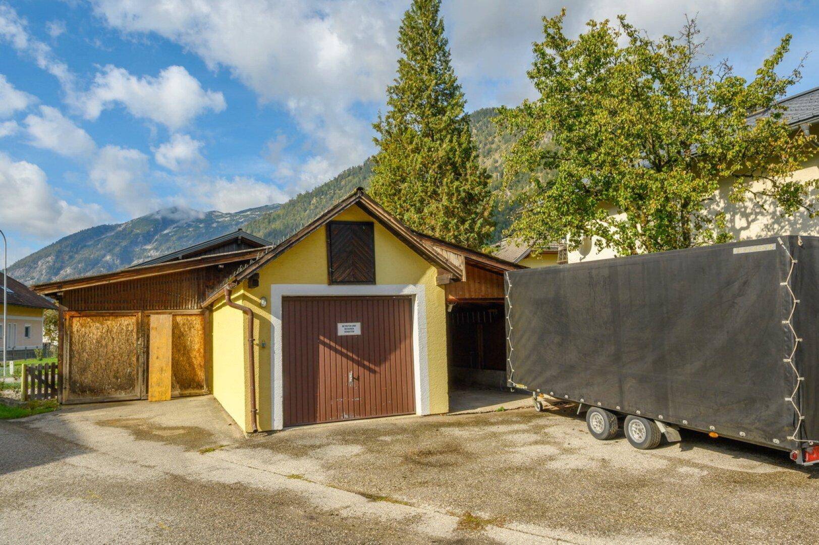 Traditionelle Garage mit Holztor und angrenzenden Nebengebäuden in ländlicher Umgebung.