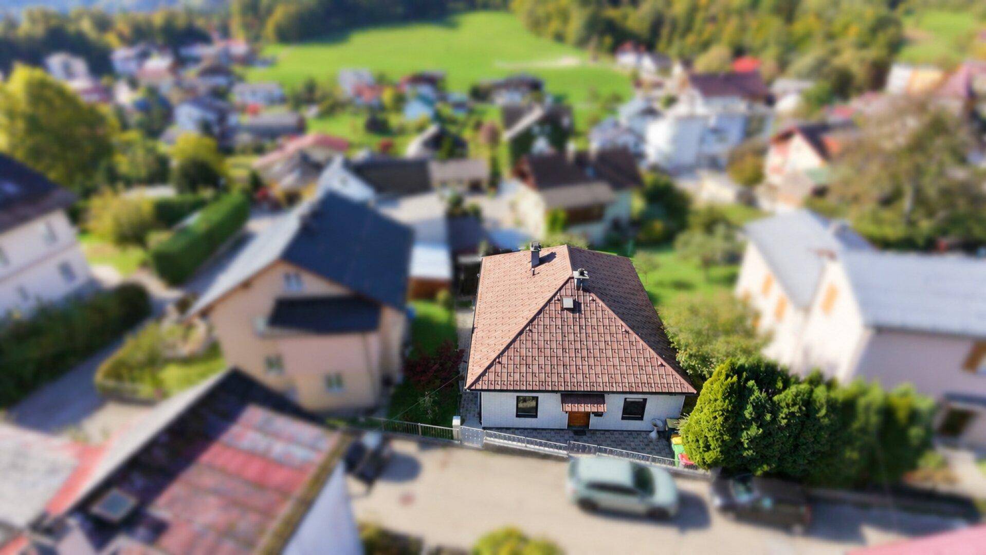 Luftaufnahme eines Einfamilienhauses mit braunem Ziegeldach in einer Wohnsiedlung.