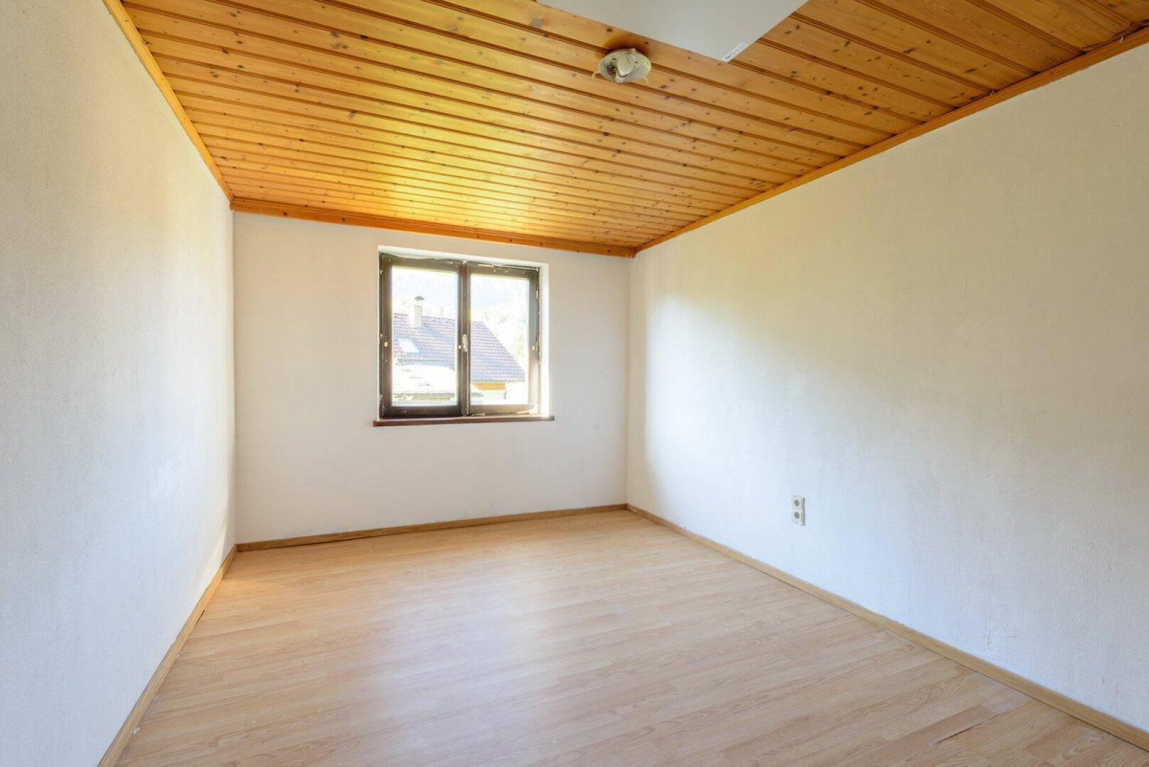 Schlafzimmer mit Holzboden, Holzdecke und einem Fenster mit Blick ins Grüne.