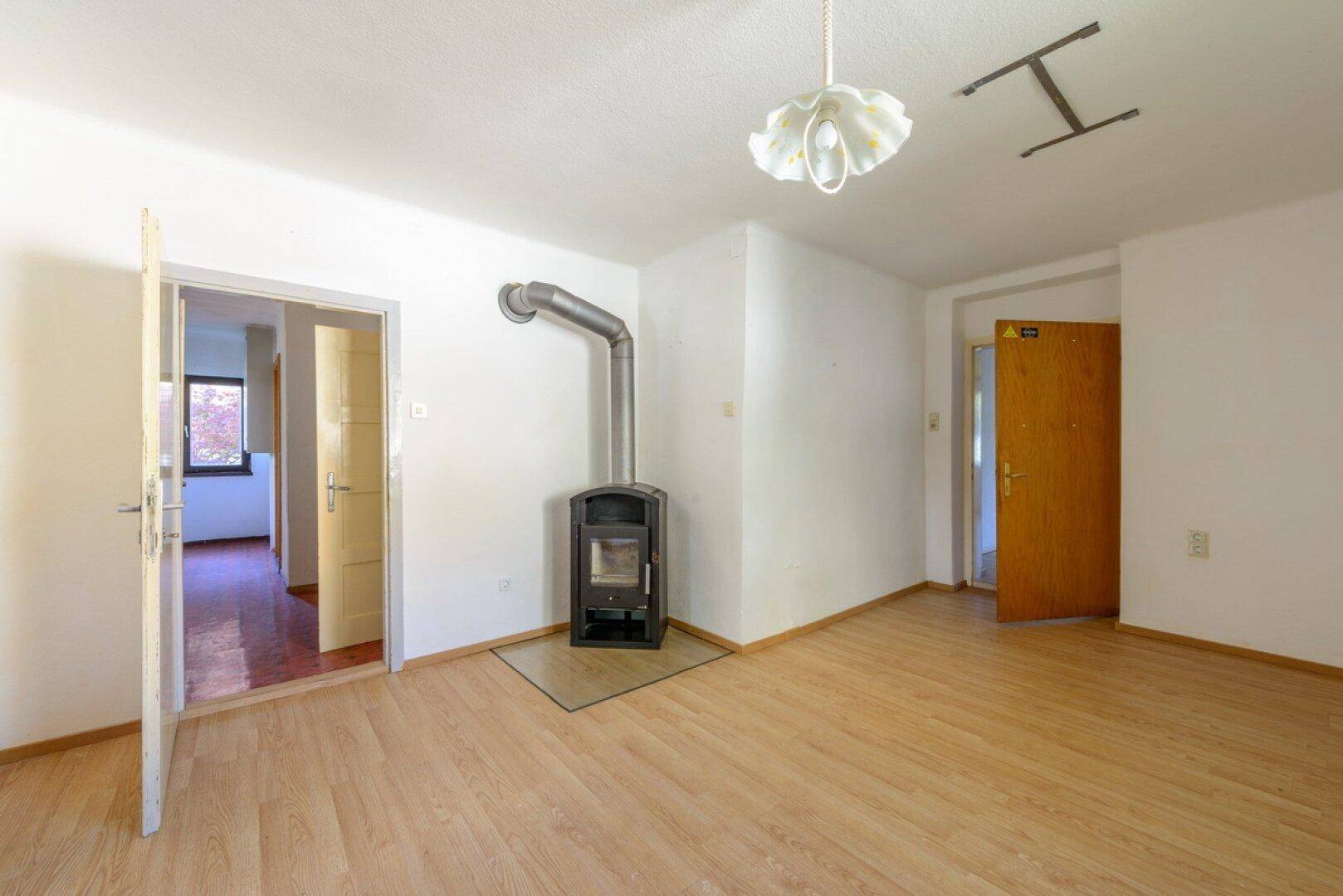 Wohnzimmer mit Holzboden, Kaminofen und Zugang zu weiteren Räumen.
