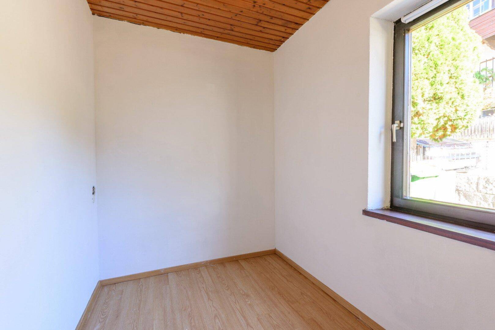 Kleiner Raum mit Holzboden, Holzdecke und einem Fenster, das Tageslicht hereinlässt.