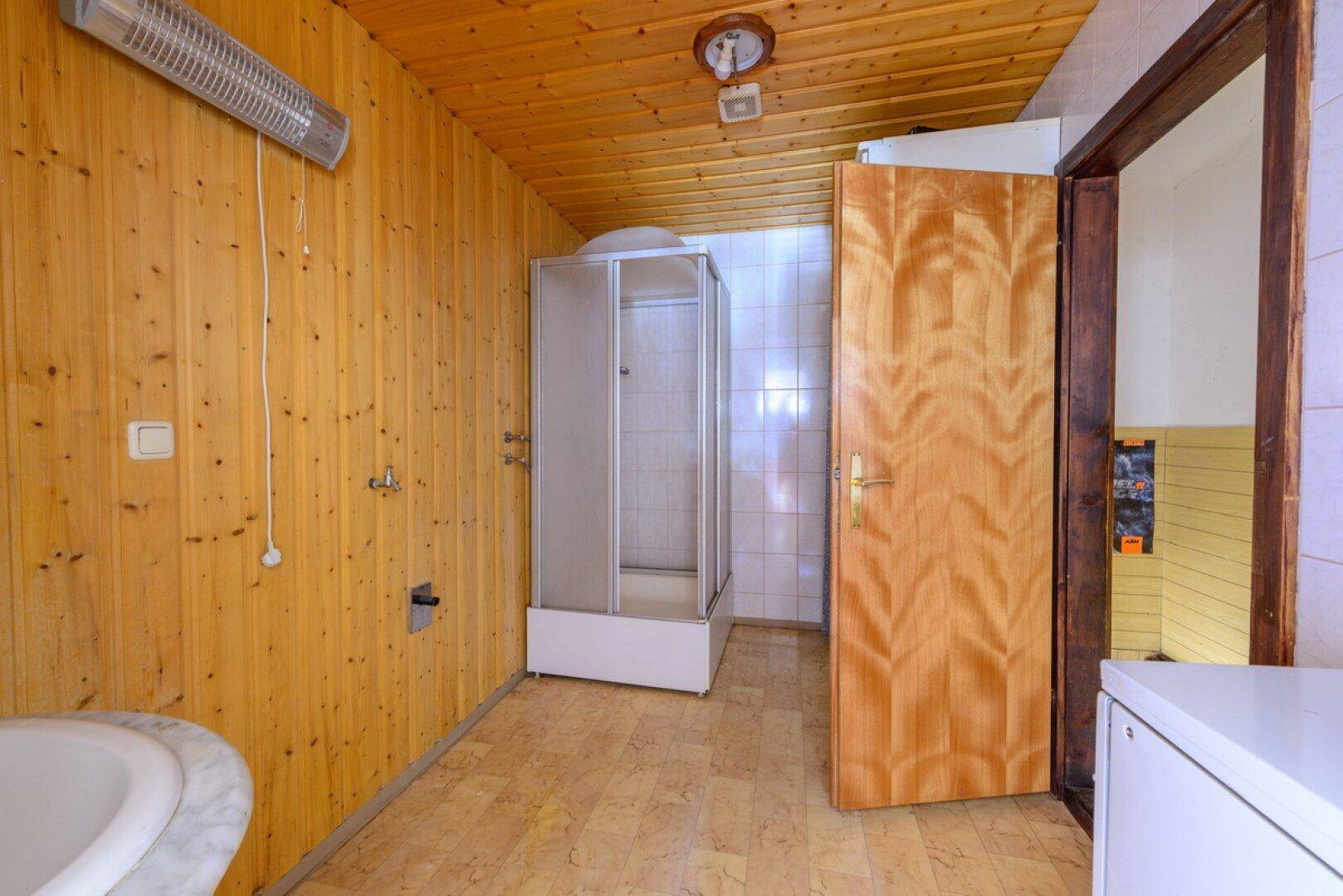 Badezimmer mit Holzvertäfelung, Duschkabine und Waschmaschinenanschluss.