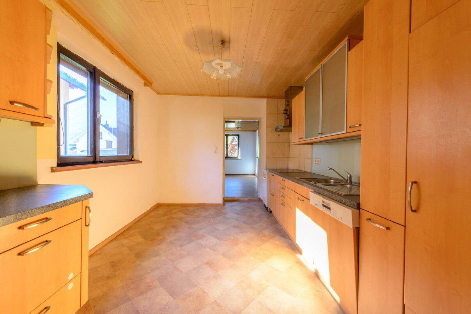 Geräumige Küche mit Holzschränken, Fliesenboden und Blick in den Flur.