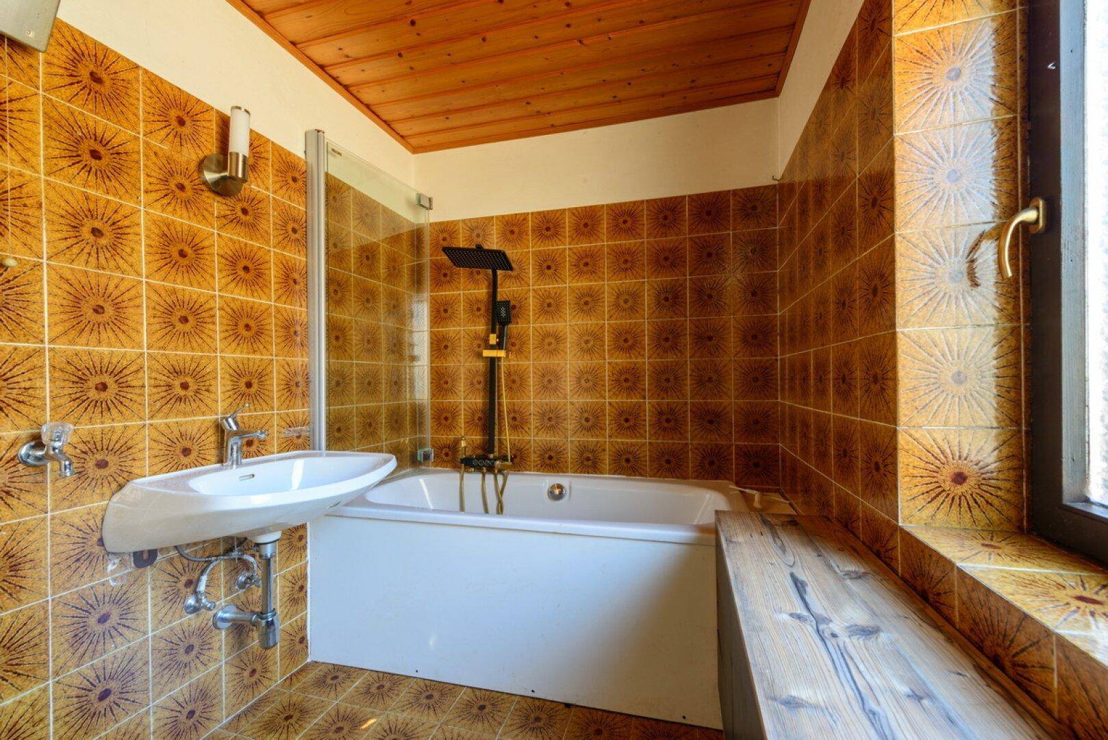 Badezimmer mit auffälligen braunen Fliesen, Badewanne, Waschbecken und Fenster.