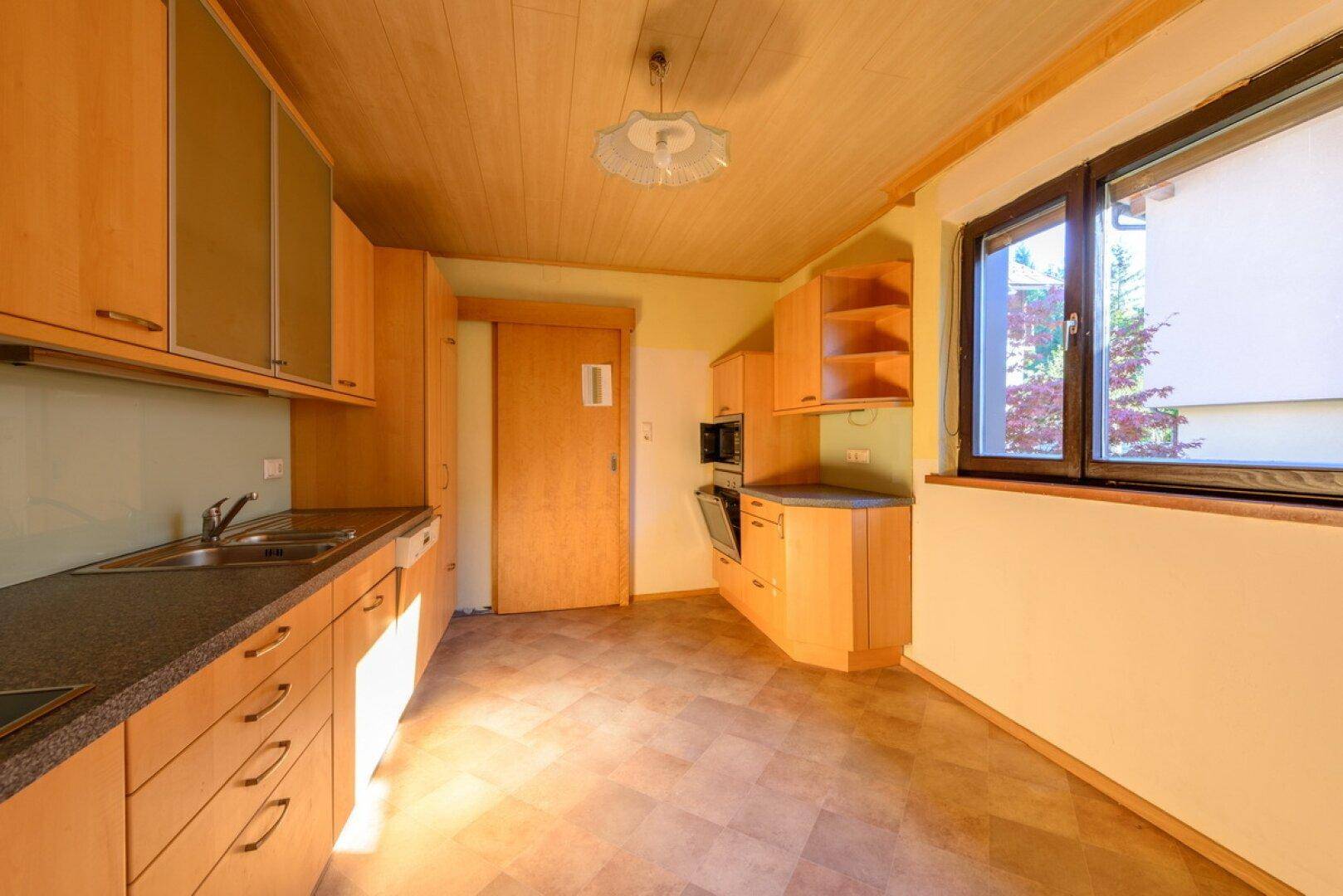 Helle Küche mit Holzvertäfelung an der Decke, Einbauschränken und Fenster.