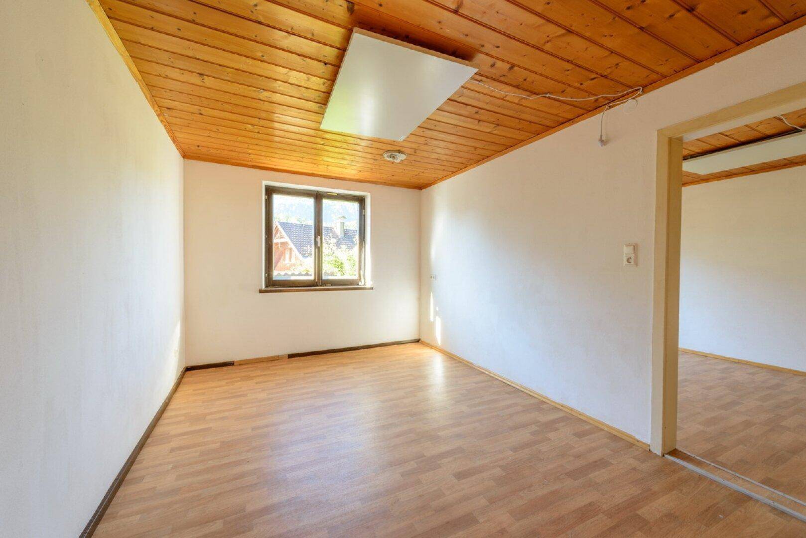 Helles Schlafzimmer mit Laminatboden, Holzdecke und Fenster, das viel Licht spendet.
