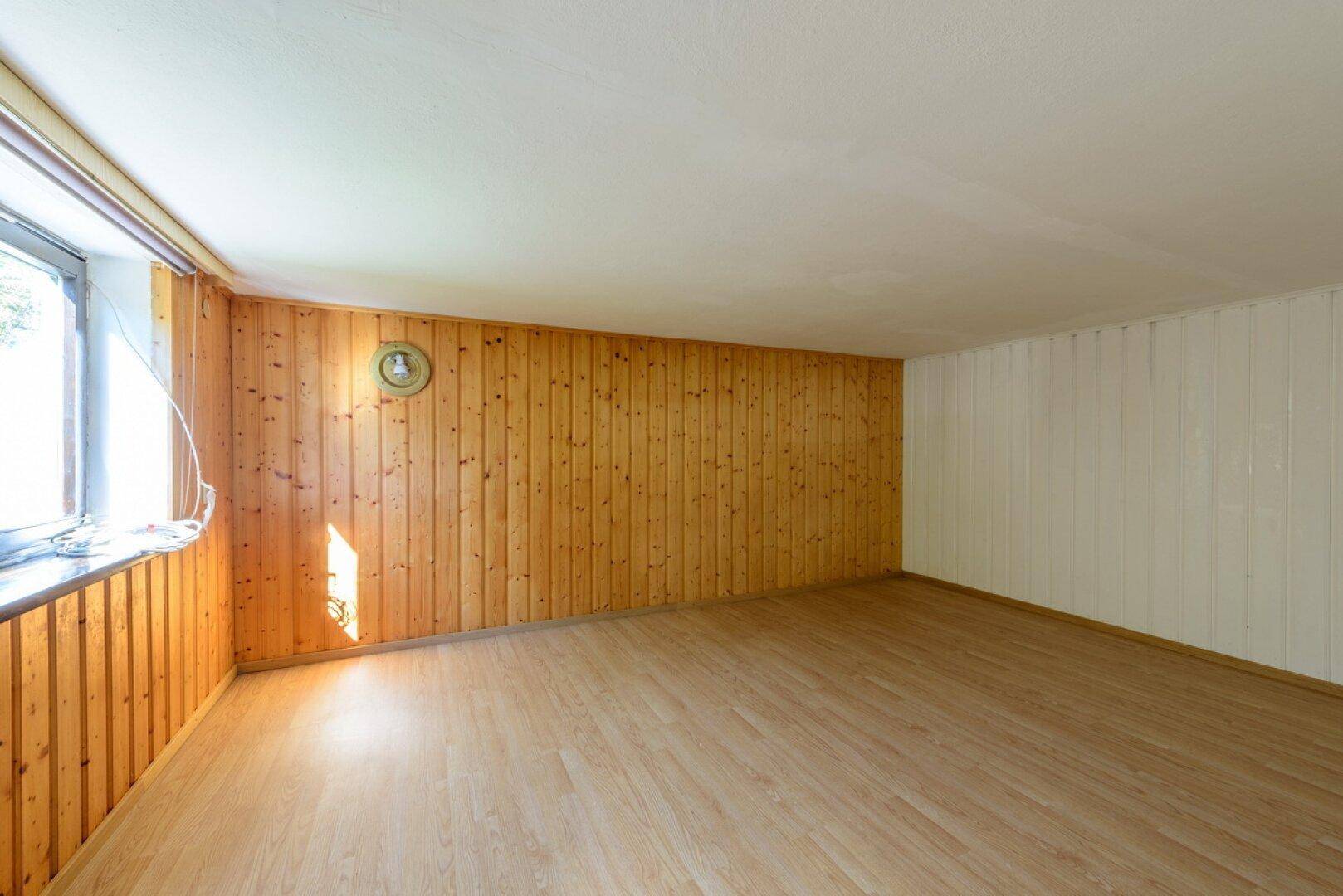 Geräumiger Raum mit Holzwandvertäfelung, Laminatboden und einem großen Fenster.