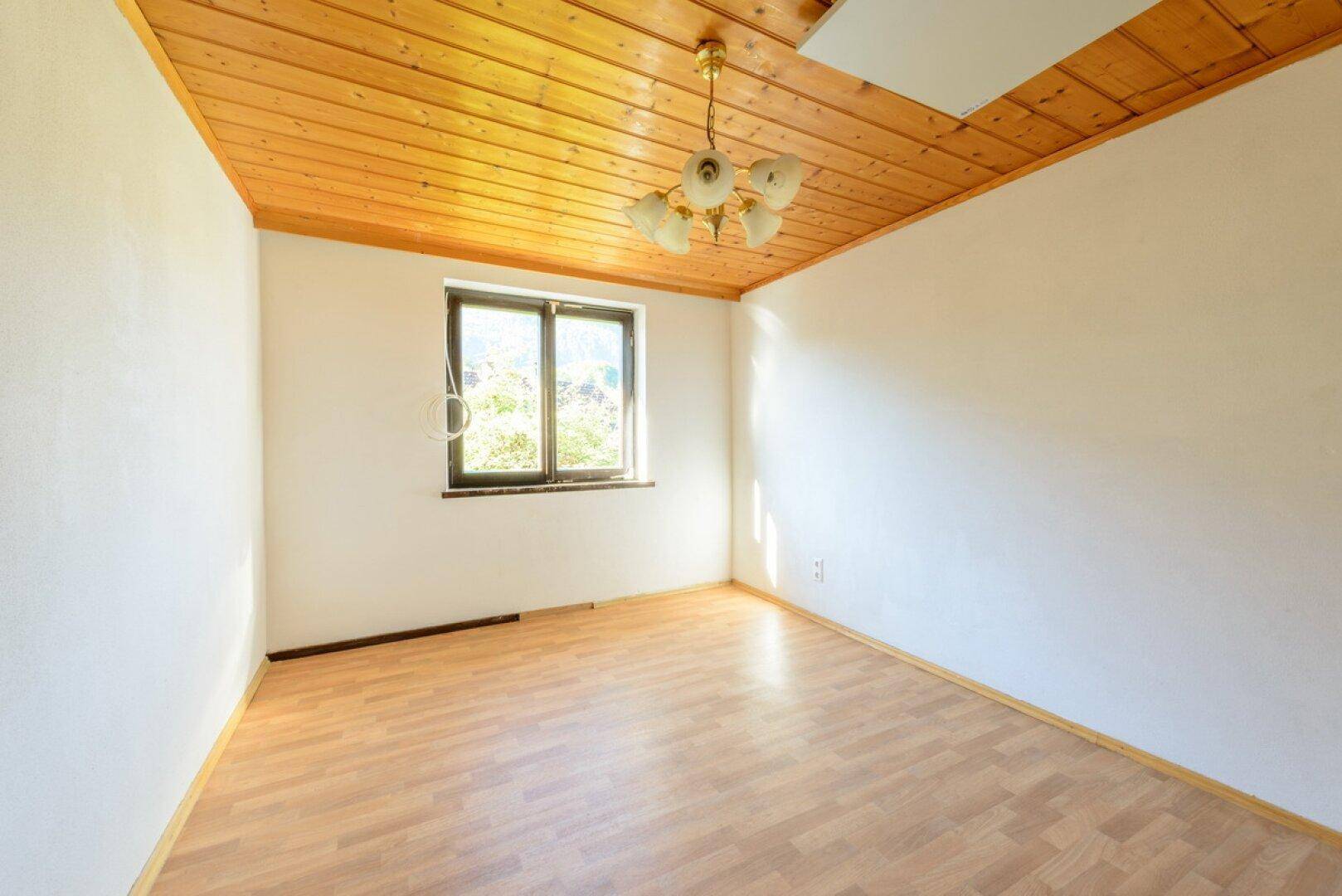 Geräumiges Schlafzimmer mit Laminatboden, Holzdecke und einem Fenster für natürliche Belichtung.