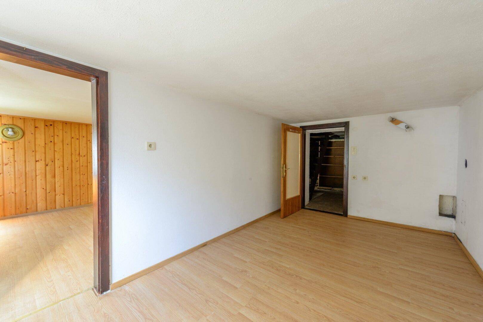 Heller Wohnraum mit Laminatboden und Holzwand, der Zugang zu weiteren Zimmern bietet.