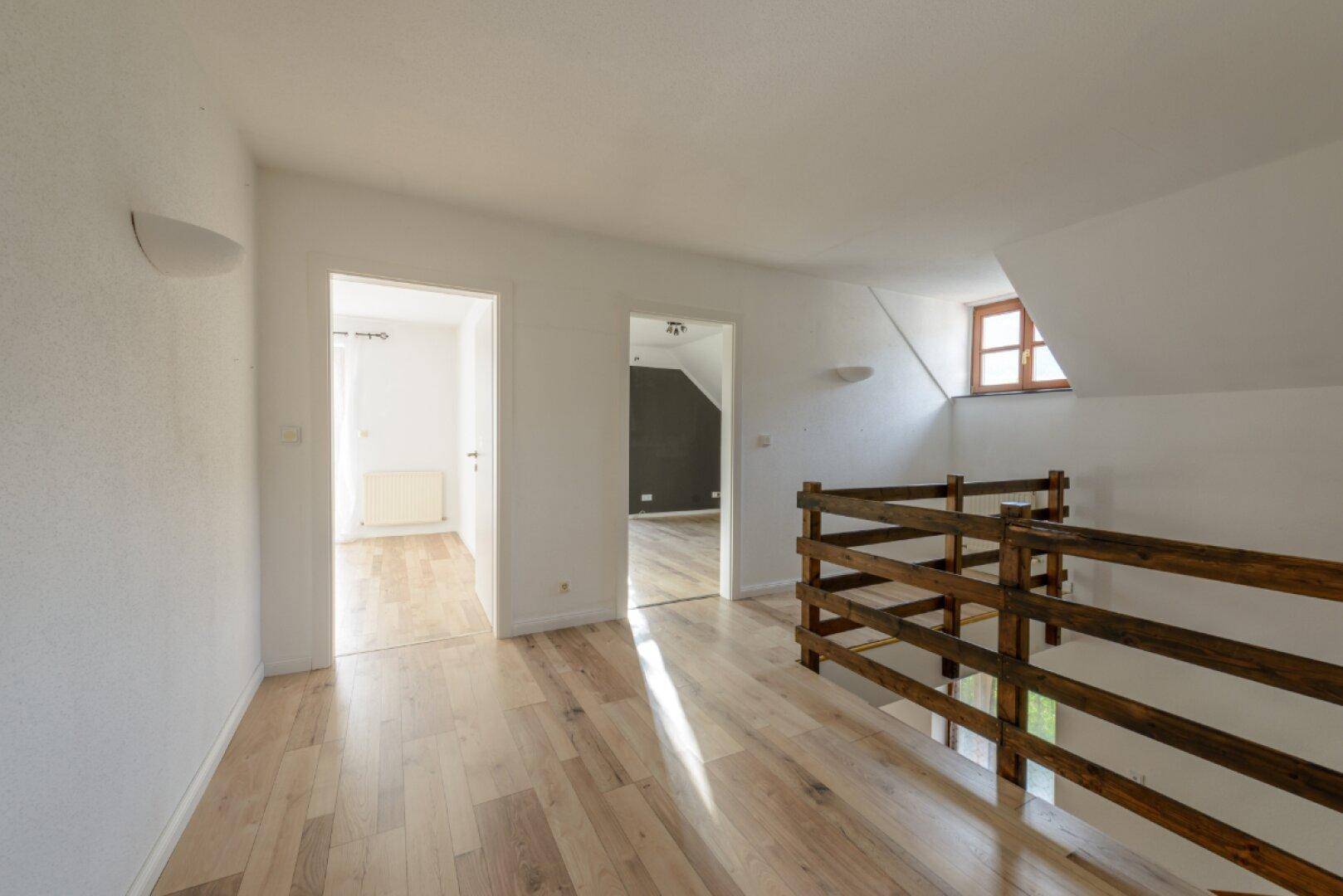 Heller Flur im Obergeschoss mit Holzboden, Holzgeländer und Zugang zu weiteren Zimmern.