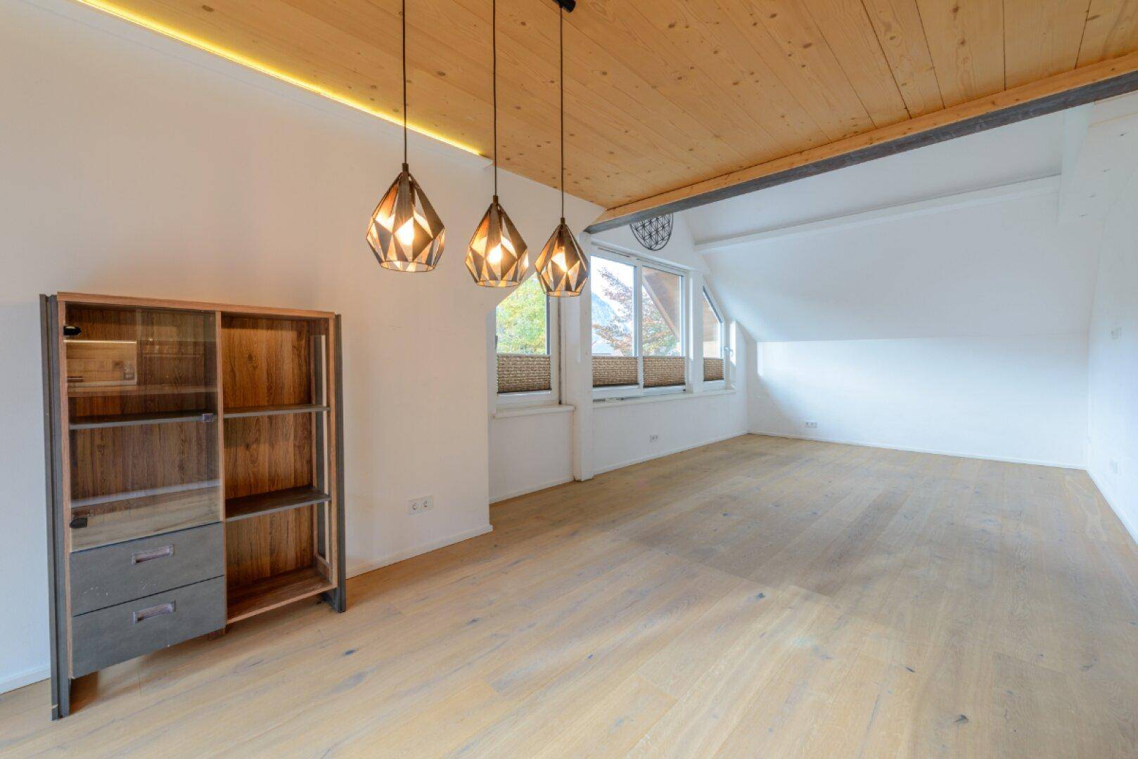 Heller Wohnbereich mit Holzboden, Holzdecke und großen Fenstern unter einer Dachschräge.