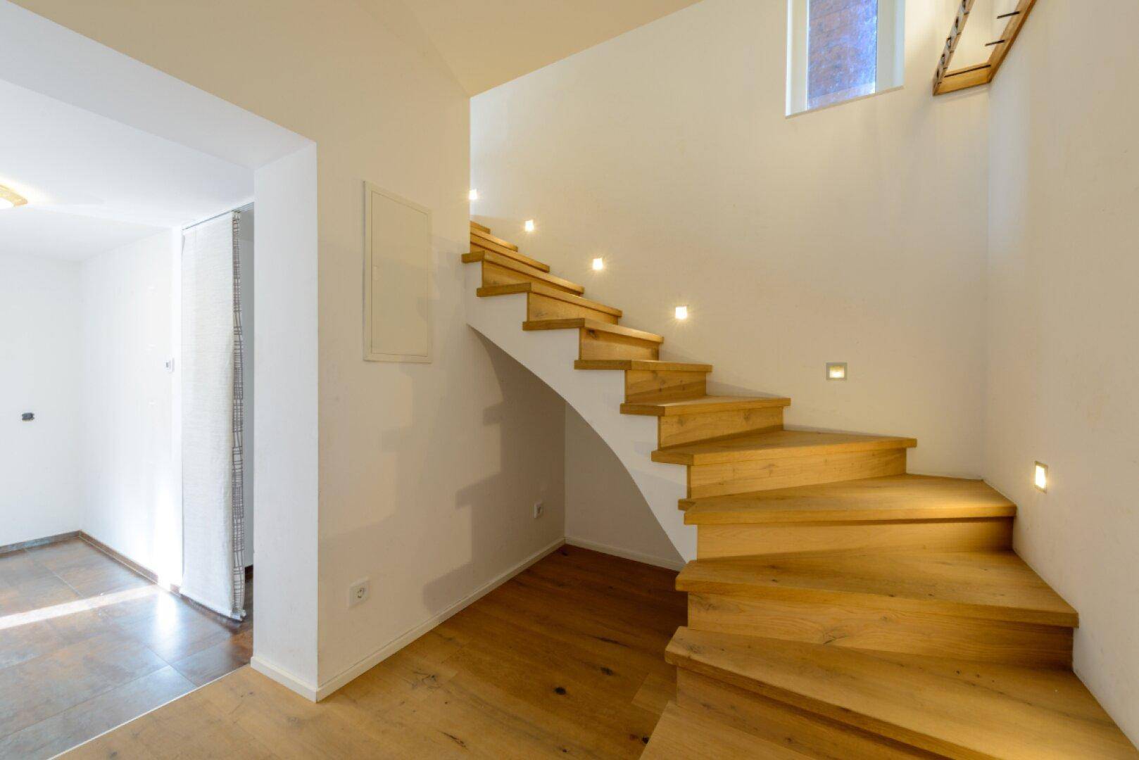 Moderne Holztreppe mit integrierter Beleuchtung, die verschiedene Etagen verbindet.