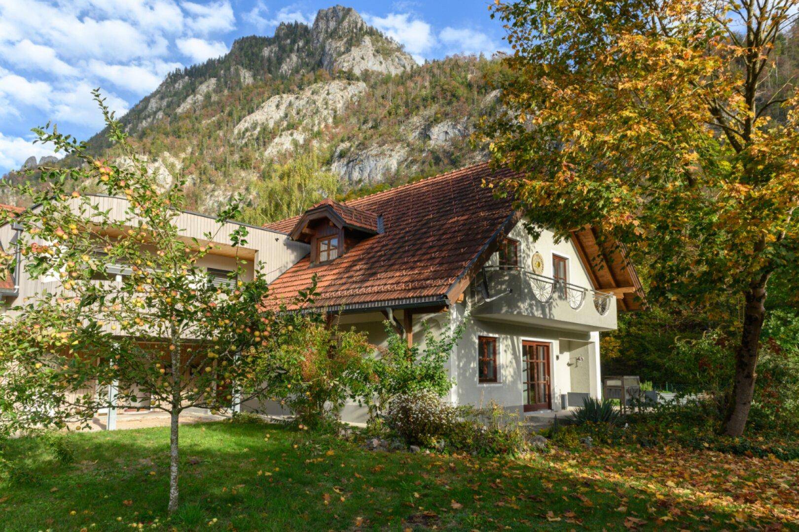 Charmantes Wohnhaus mit Ziegeldach und Garten umgeben von herbstlicher Natur und Bergen.
