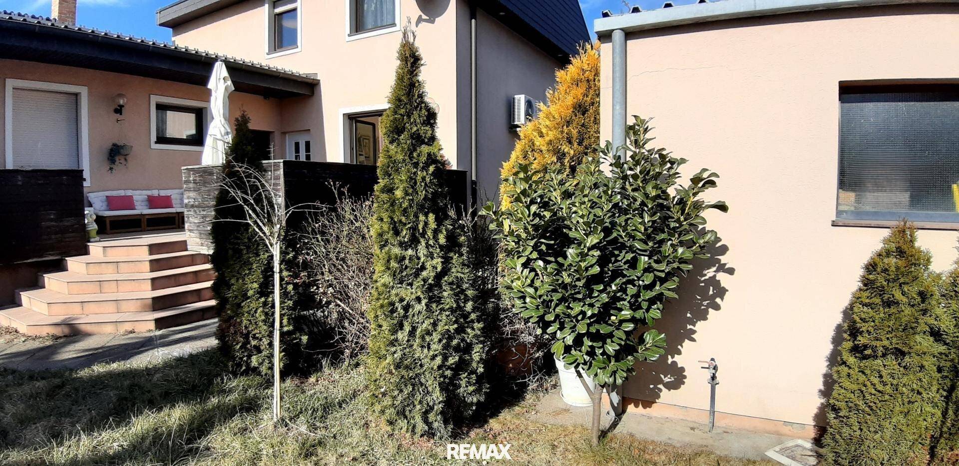 Seitenansicht des Hauses mit gepflegten Sträuchern, einer Außentreppe und einer hellen Fassade.