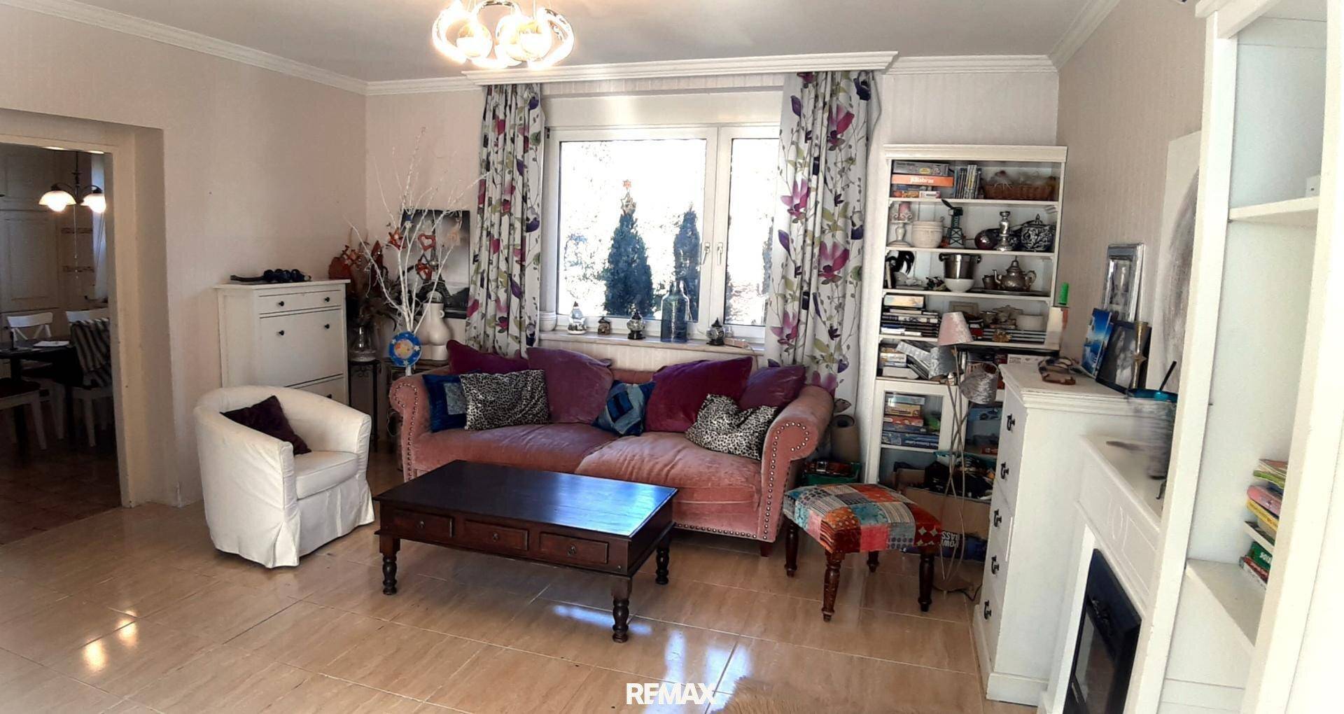 Geräumiges Wohnzimmer mit Sofa, Bücherregal und hellem Fliesenboden.
