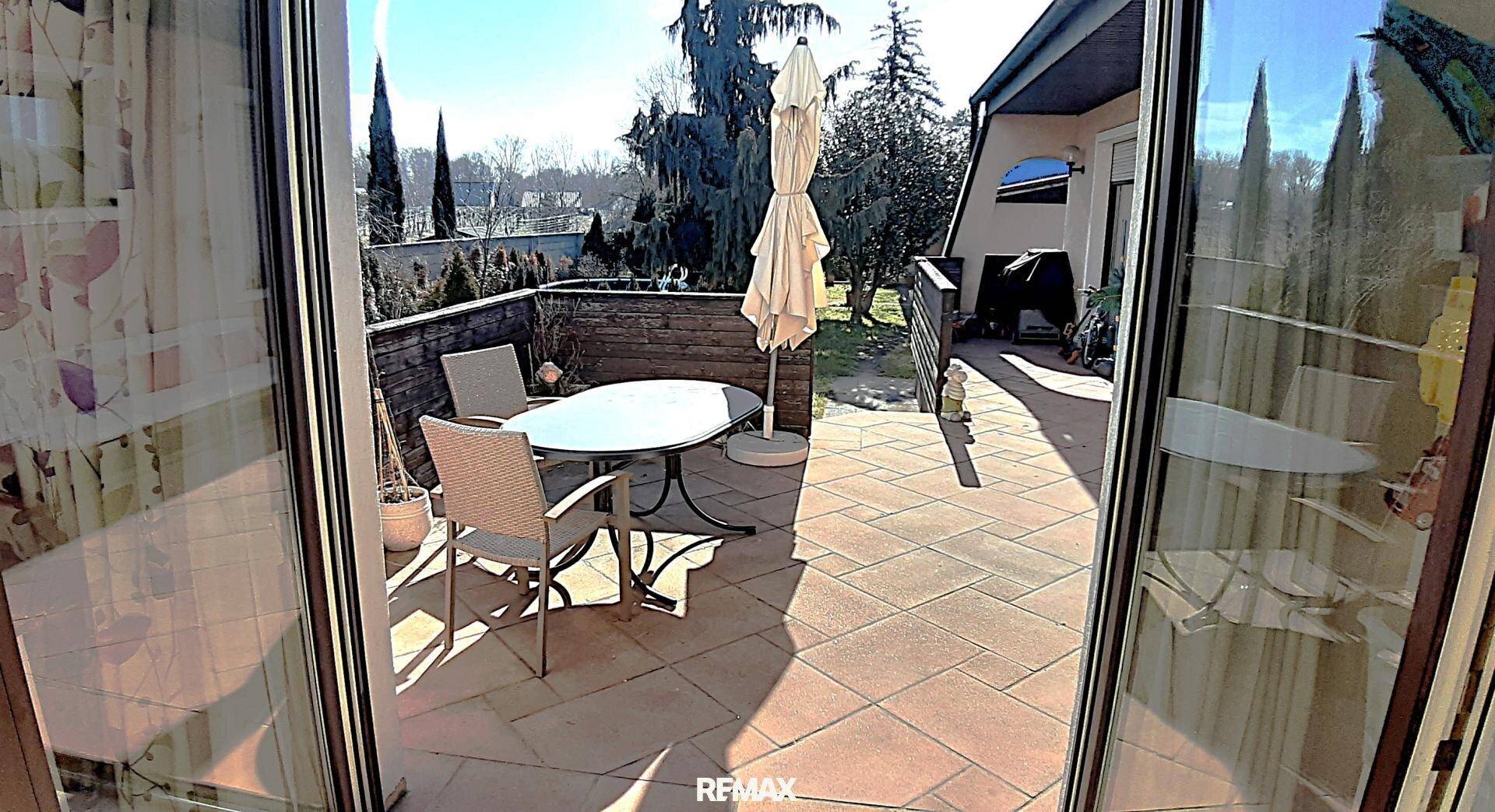 Sonniger Terrassenbereich mit Esstisch und Sonnenschirm, ideal für Mahlzeiten im Freien.