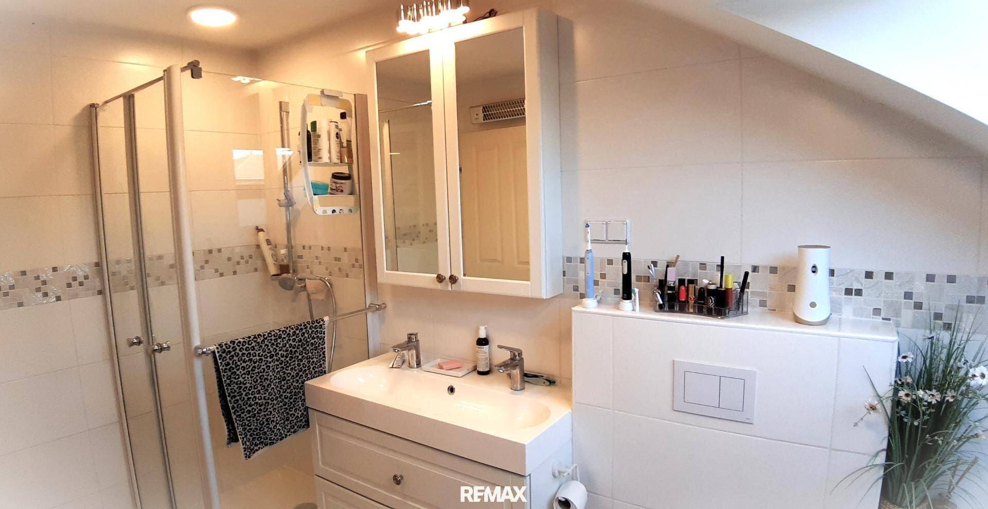 Modernes Badezimmer im Dachgeschoss mit Duschkabine, Waschbecken und Spiegelschrank.