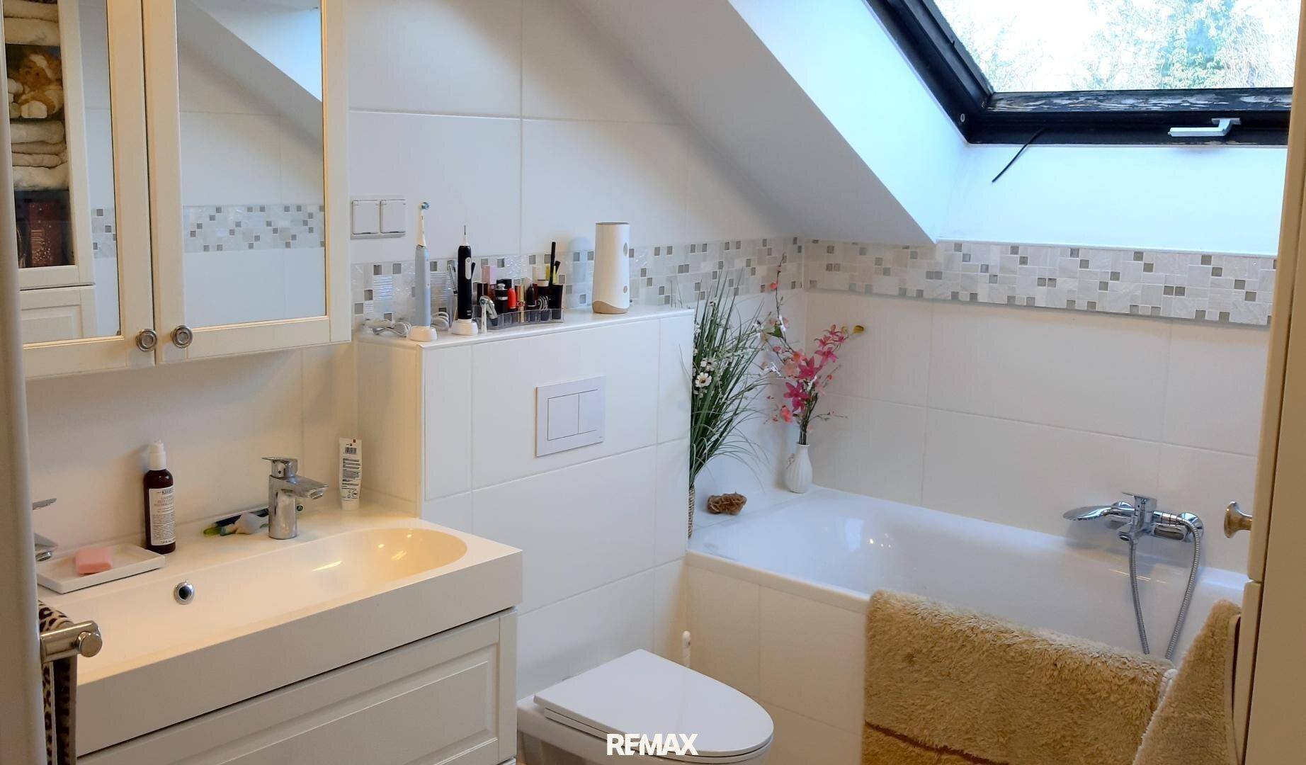 Helles Badezimmer mit Badewanne, Dachfenster und modernen weißen Fliesen, die für eine saubere Optik sorgen.