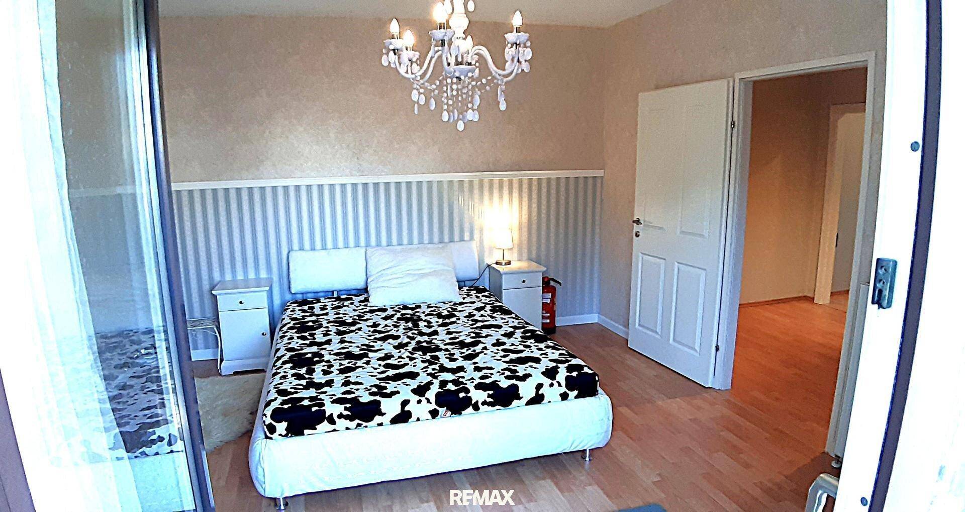 Gemütliches Schlafzimmer mit Holzboden, großem Bett, Nachttischen und einem dekorativen Kronleuchter an der Decke.