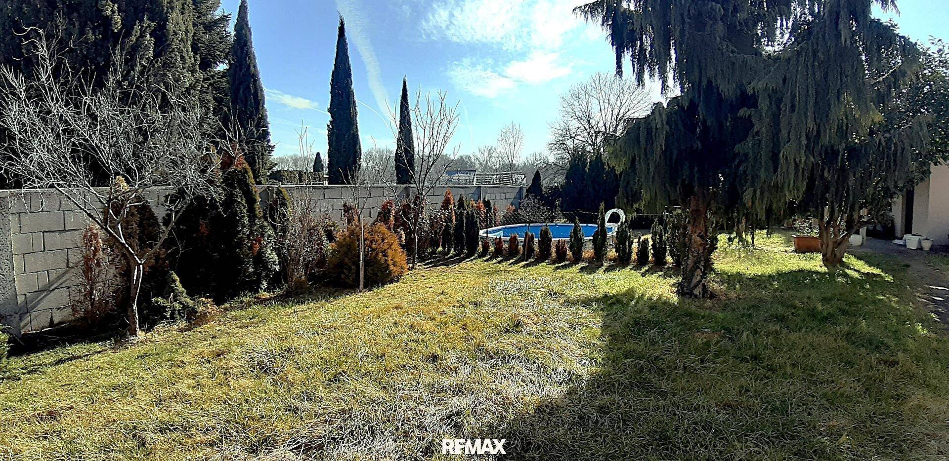 Großer Garten mit Rasenfläche, Bäumen und einem kleinen Pool im Hintergrund.
