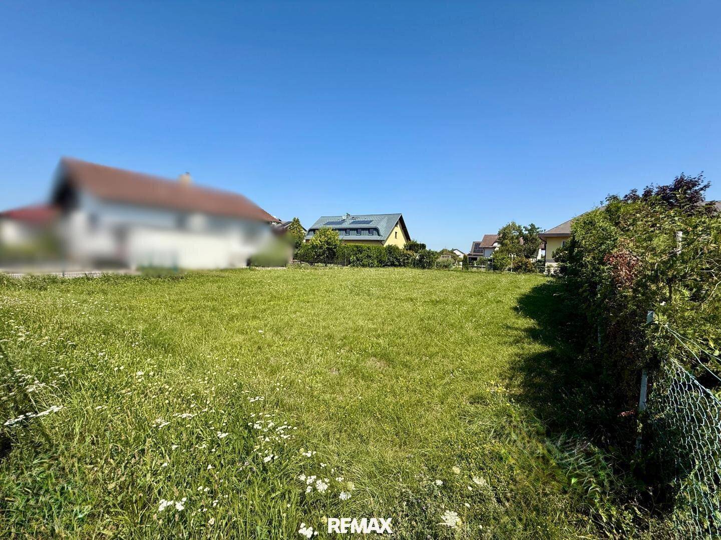 Großes, sonniges Grundstück mit viel Grünfläche und Blick auf umliegende Häuser in ländlicher Umgebung.