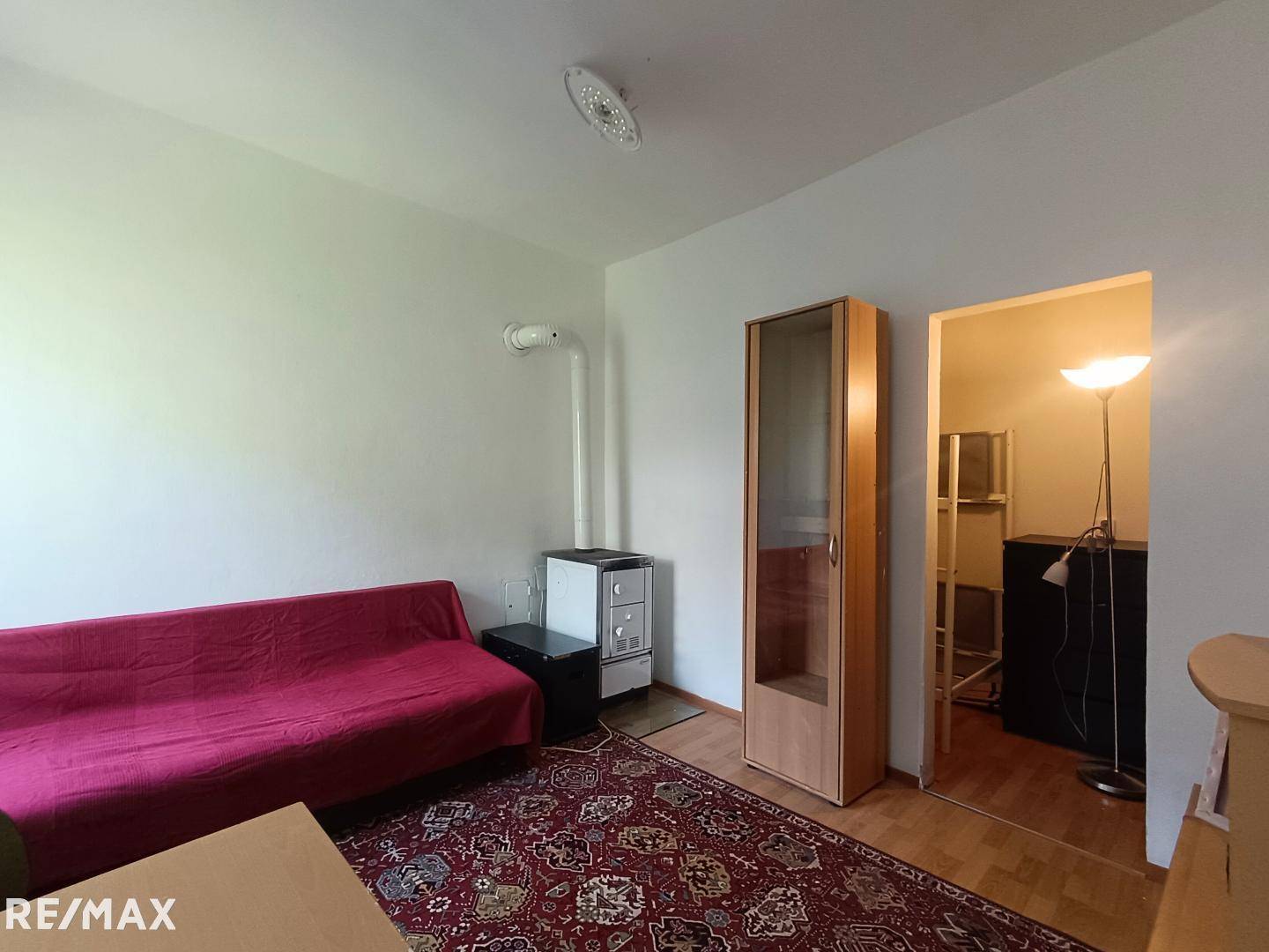 Gemütliches Wohnzimmer mit rotem Sofa, Teppichboden und einem traditionellen Holzofen.