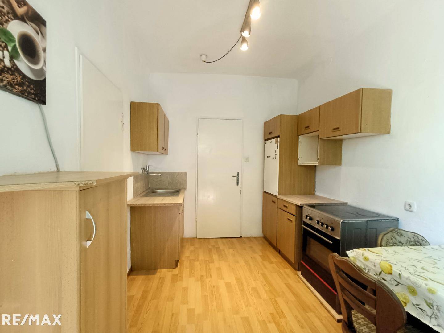 Einfache Küche mit Holzschränken, Spüle, Herd und Kühlschrank, ideal für den täglichen Gebrauch.