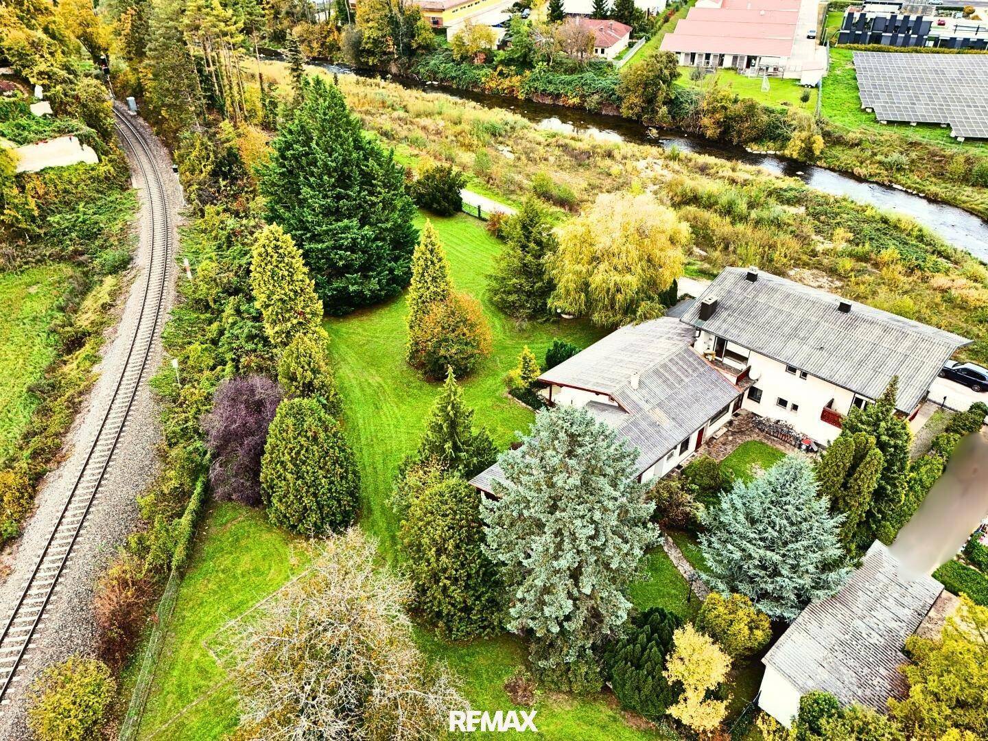 Luftaufnahme eines Anwesens mit großem Garten, angrenzenden Bahngleisen und einem Fluss in ländlicher Umgebung.