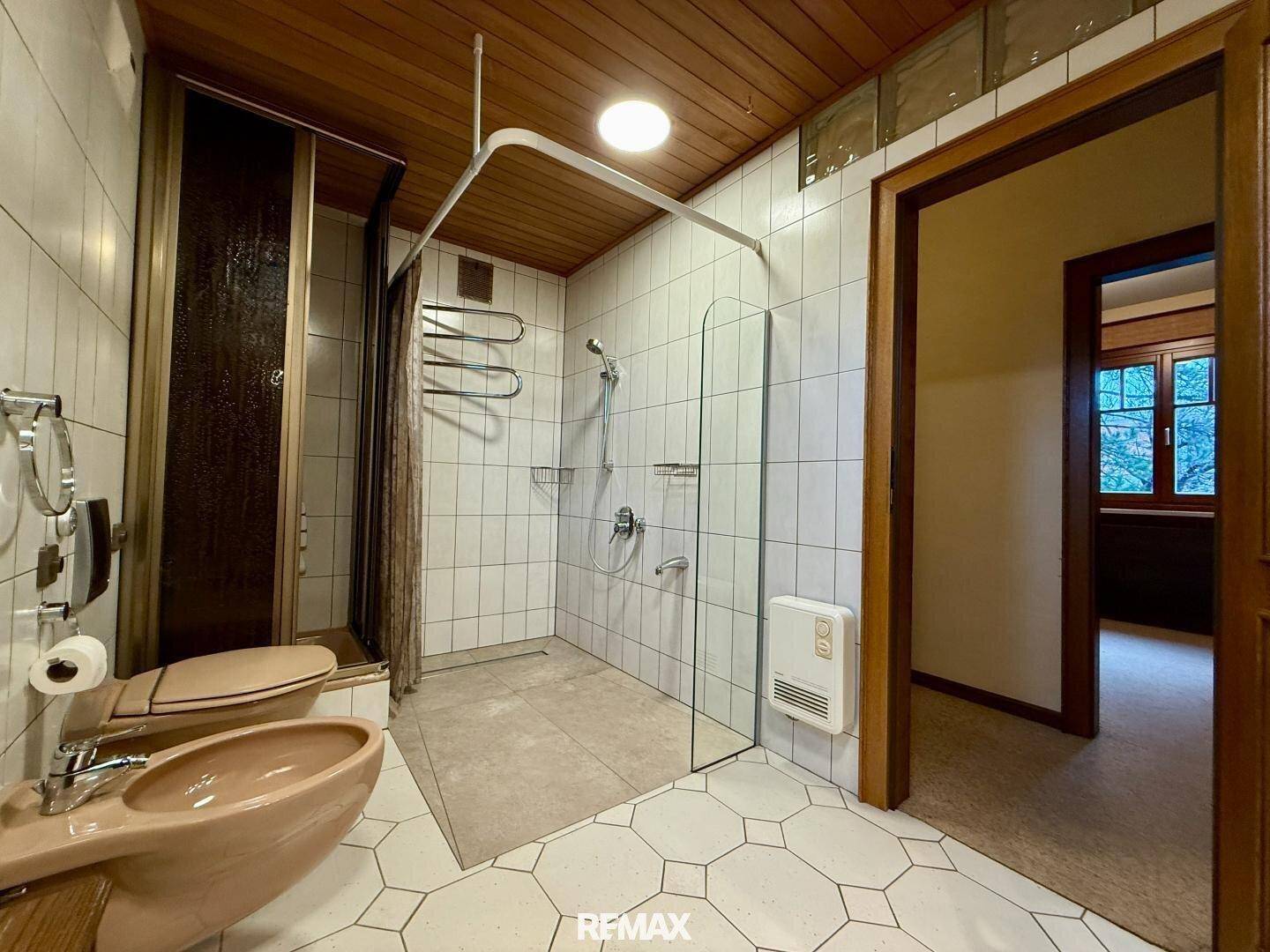 Badezimmer mit begehbarer Dusche, Bidet und Fliesen an Wänden und Boden.