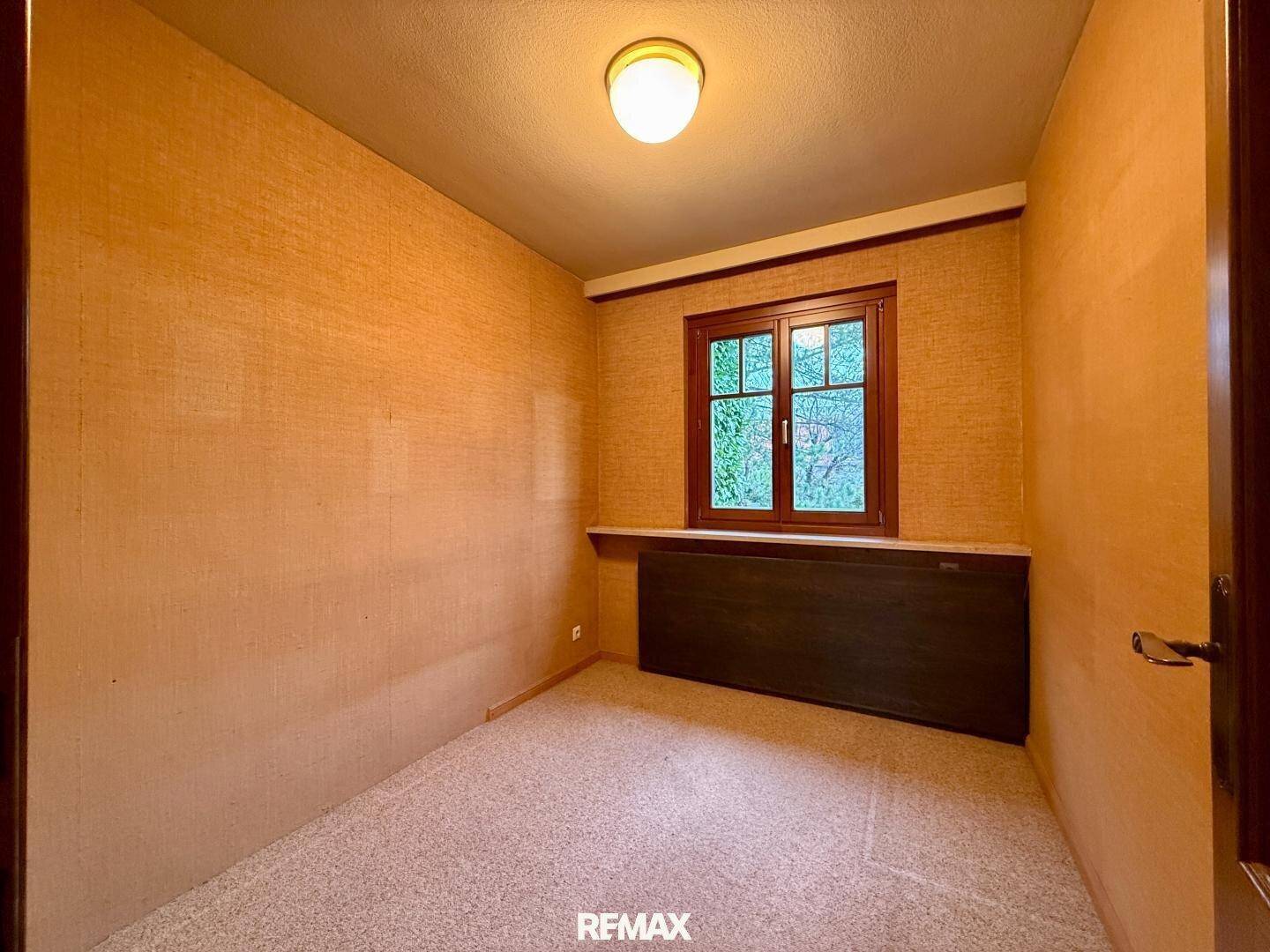 Kleines Schlafzimmer mit gemusterter Tapete, Teppichboden und Holzfenster.