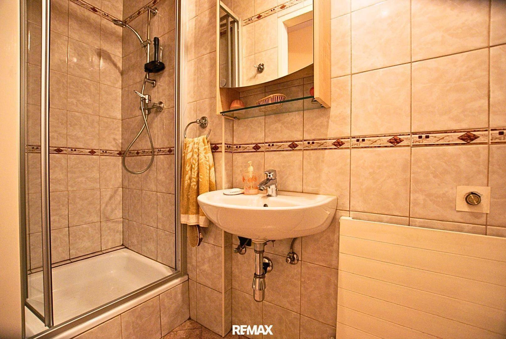 Gefliestes Badezimmer mit Duschwanne, Waschbecken und Spiegelschrank.