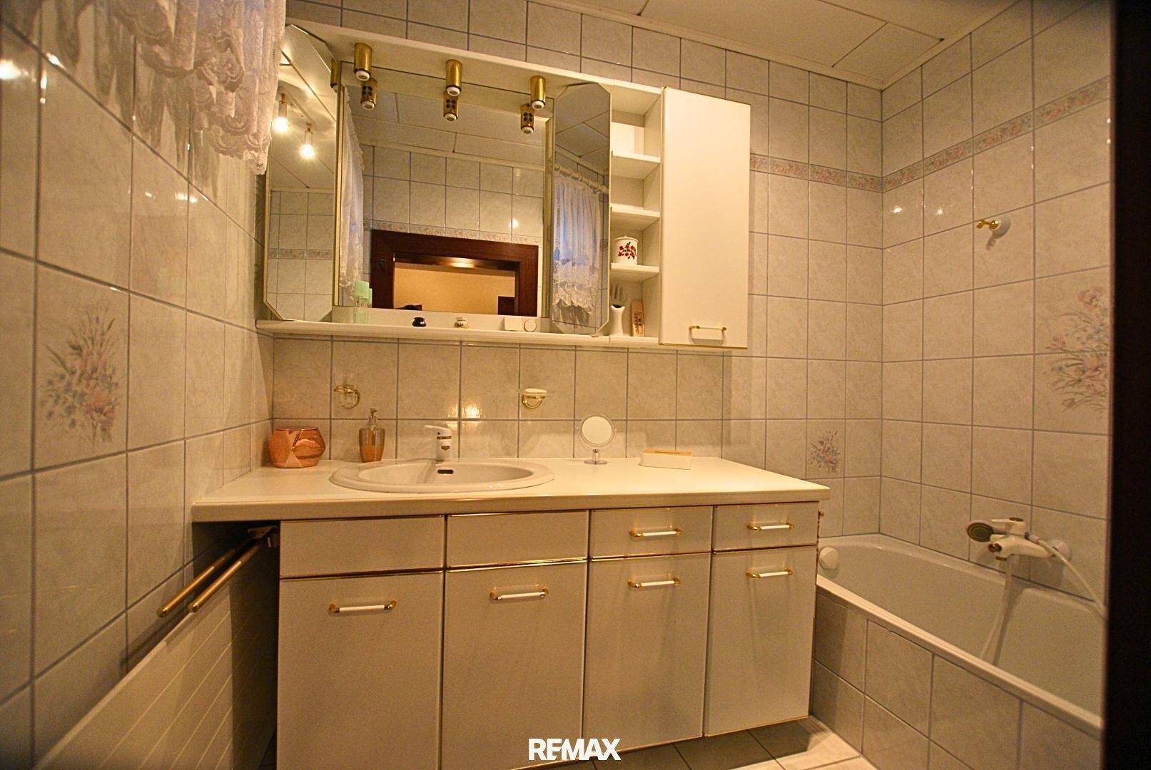 Badezimmer mit Badewanne, Waschbecken und Spiegelschrank, komplett gefliest in hellen Tönen.